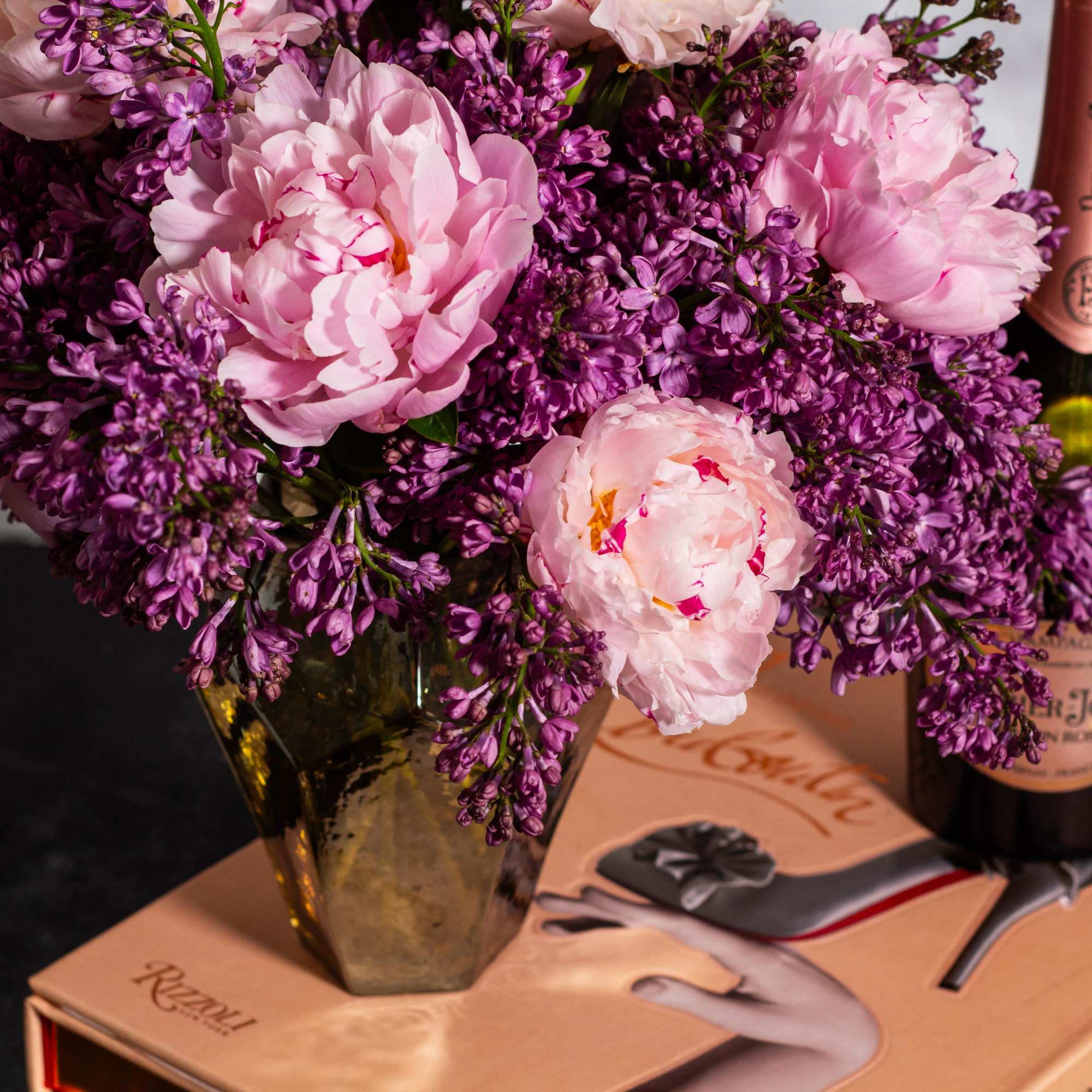The beautiful arrangement features blush color peonies and purple lilacs gathered together