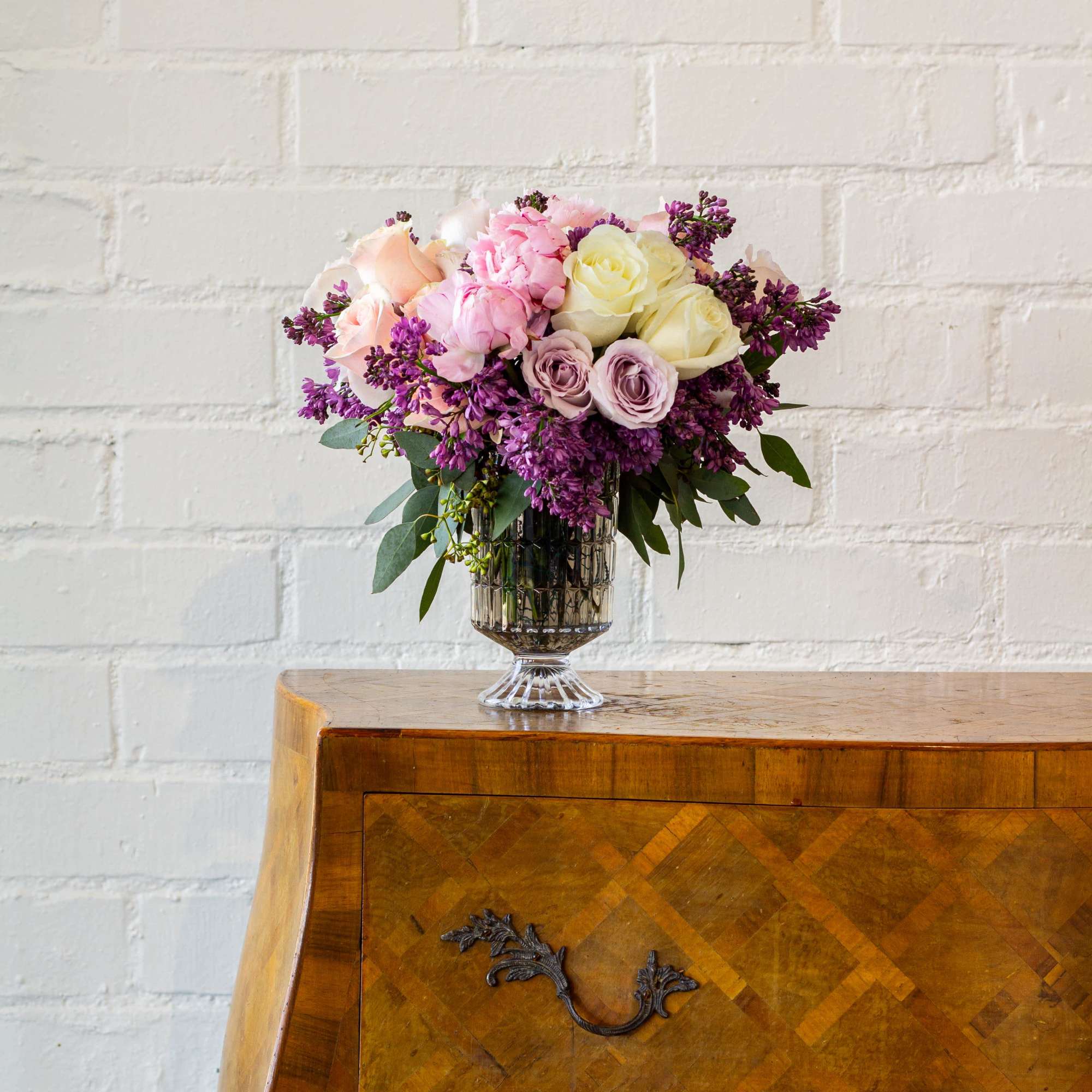 The luxurious floral arrangement features peonies, spray roses, and lilac artfully arranged