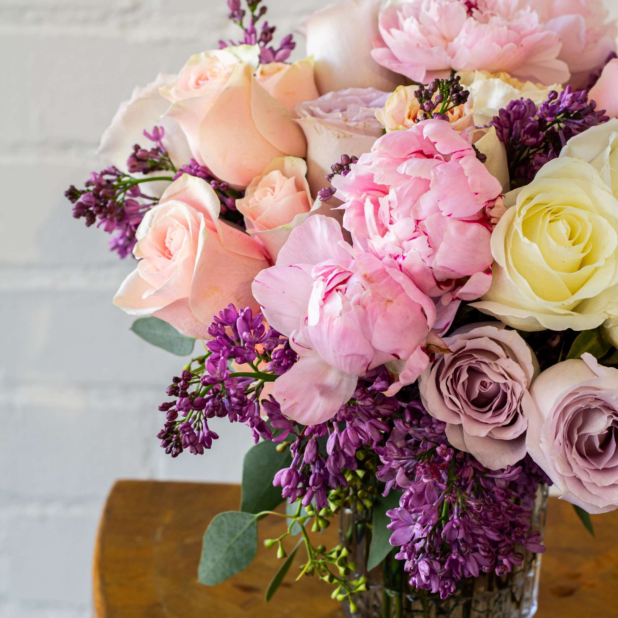 The luxurious floral arrangement features peonies, spray roses, and lilac artfully arranged