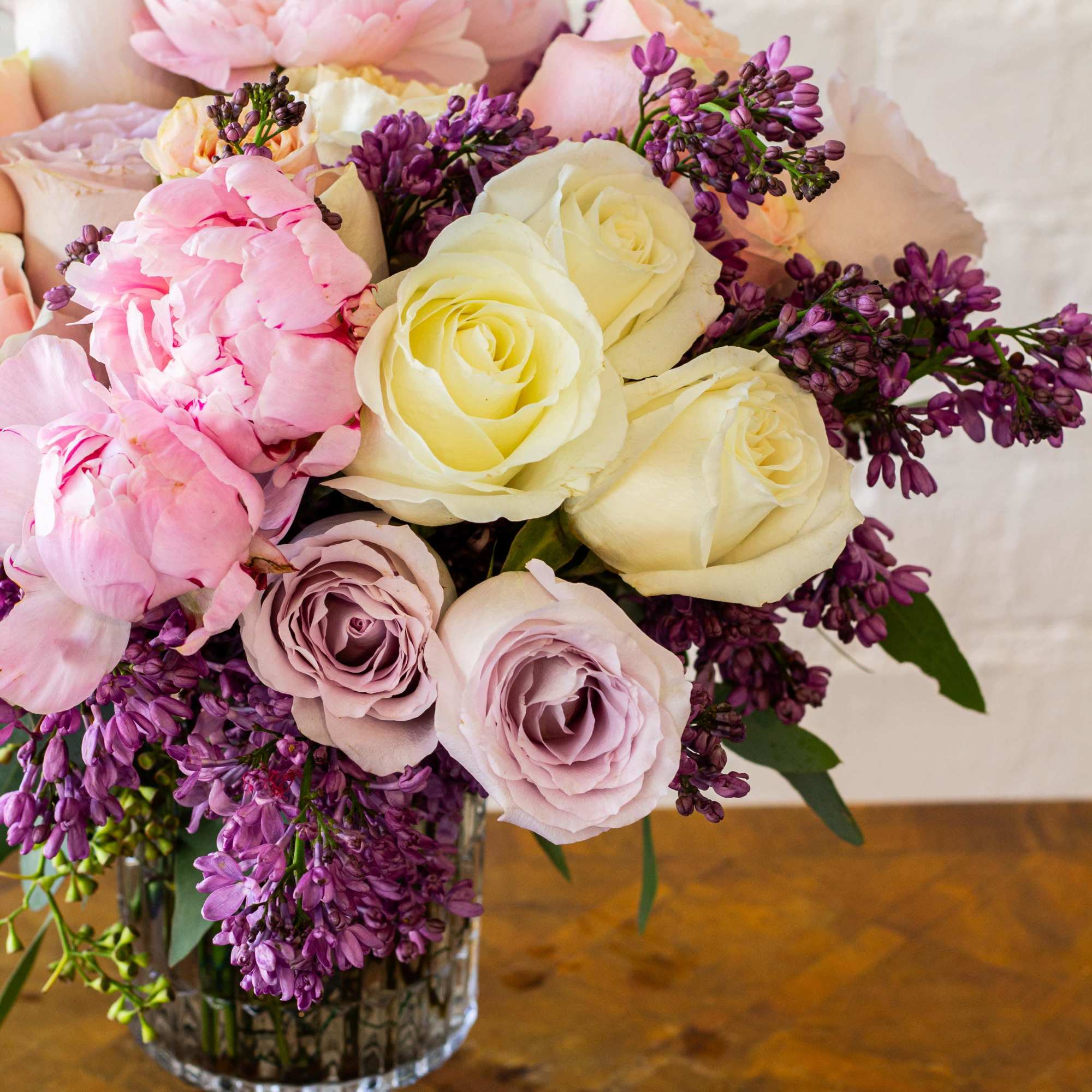 The luxurious floral arrangement features peonies, spray roses, and lilac artfully arranged