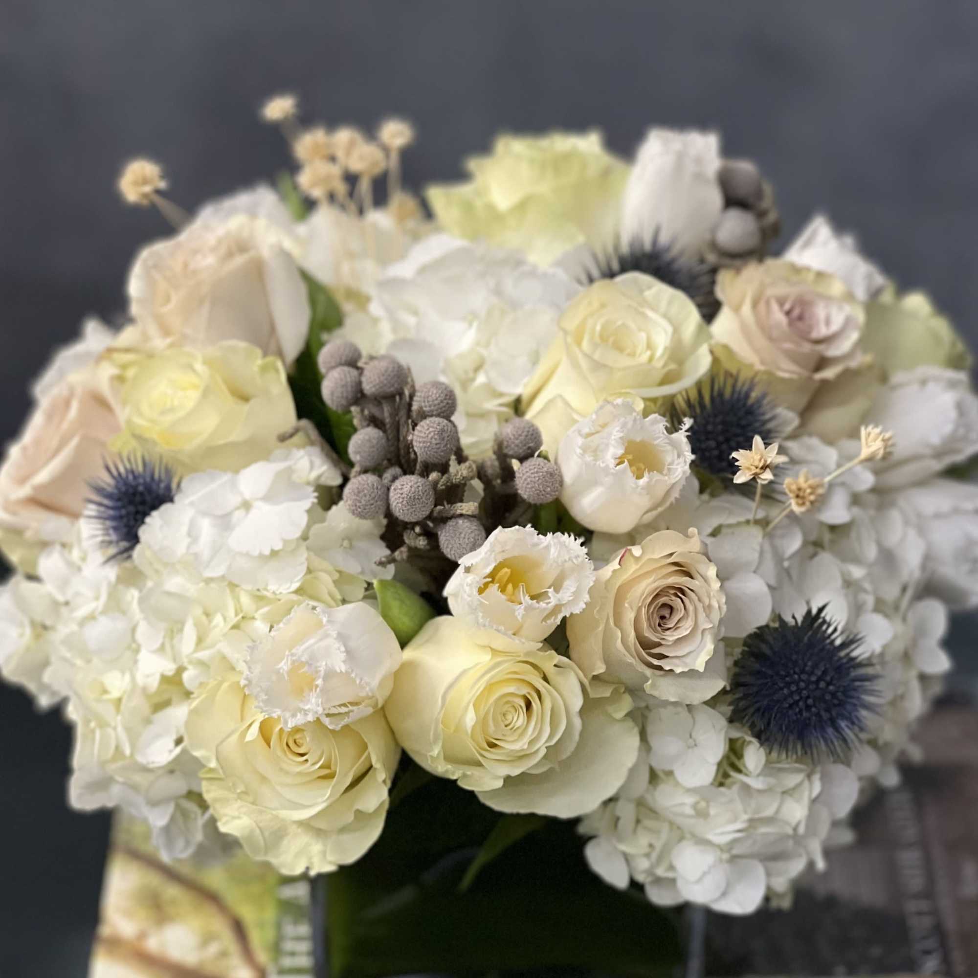 Our beautiful arrangement consists of White Roses, Hydrangeas, Thistles, Cream Roses placed