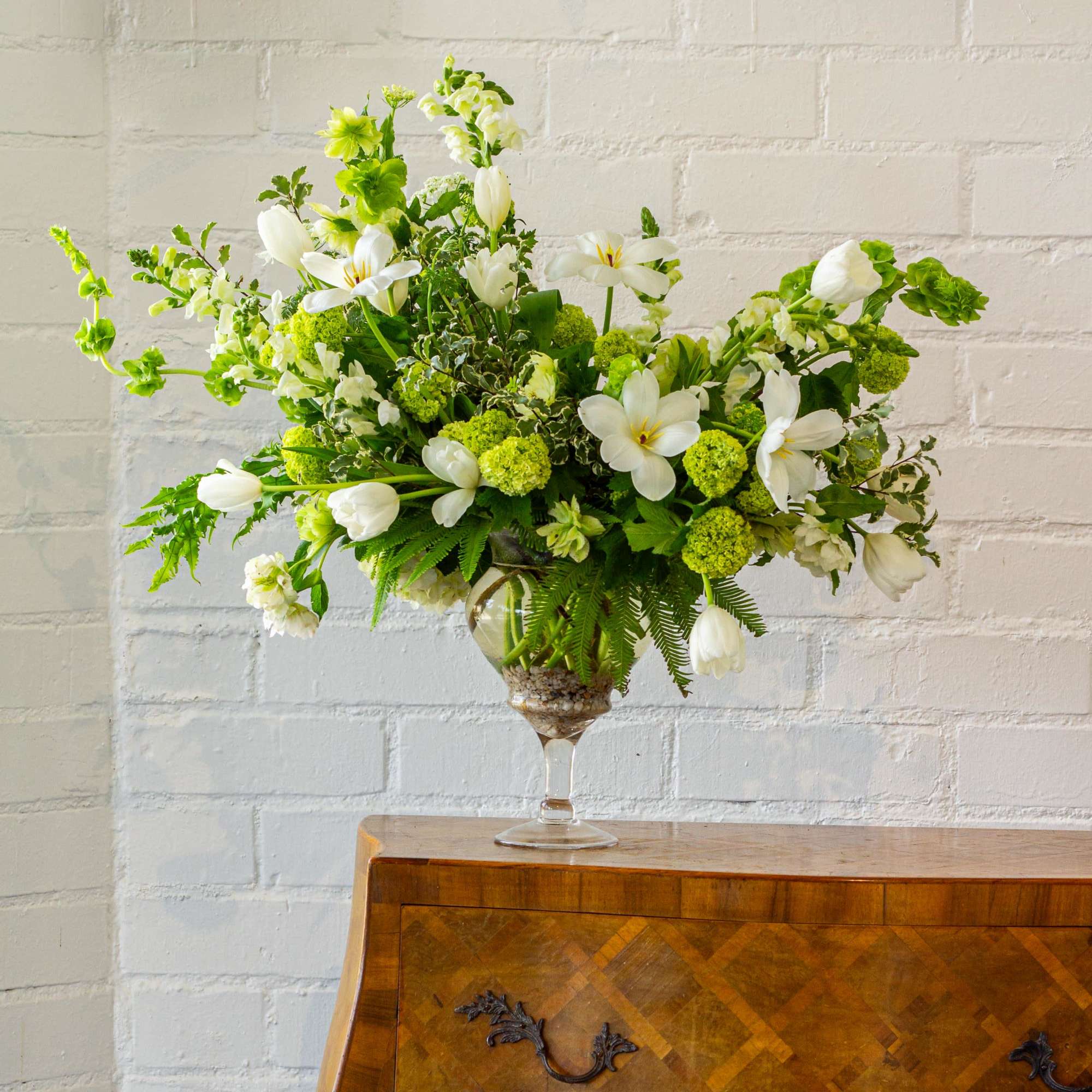 The beautiful arrangement features long white tulips, snapdragons, boulevard beautiful umbrella ferns