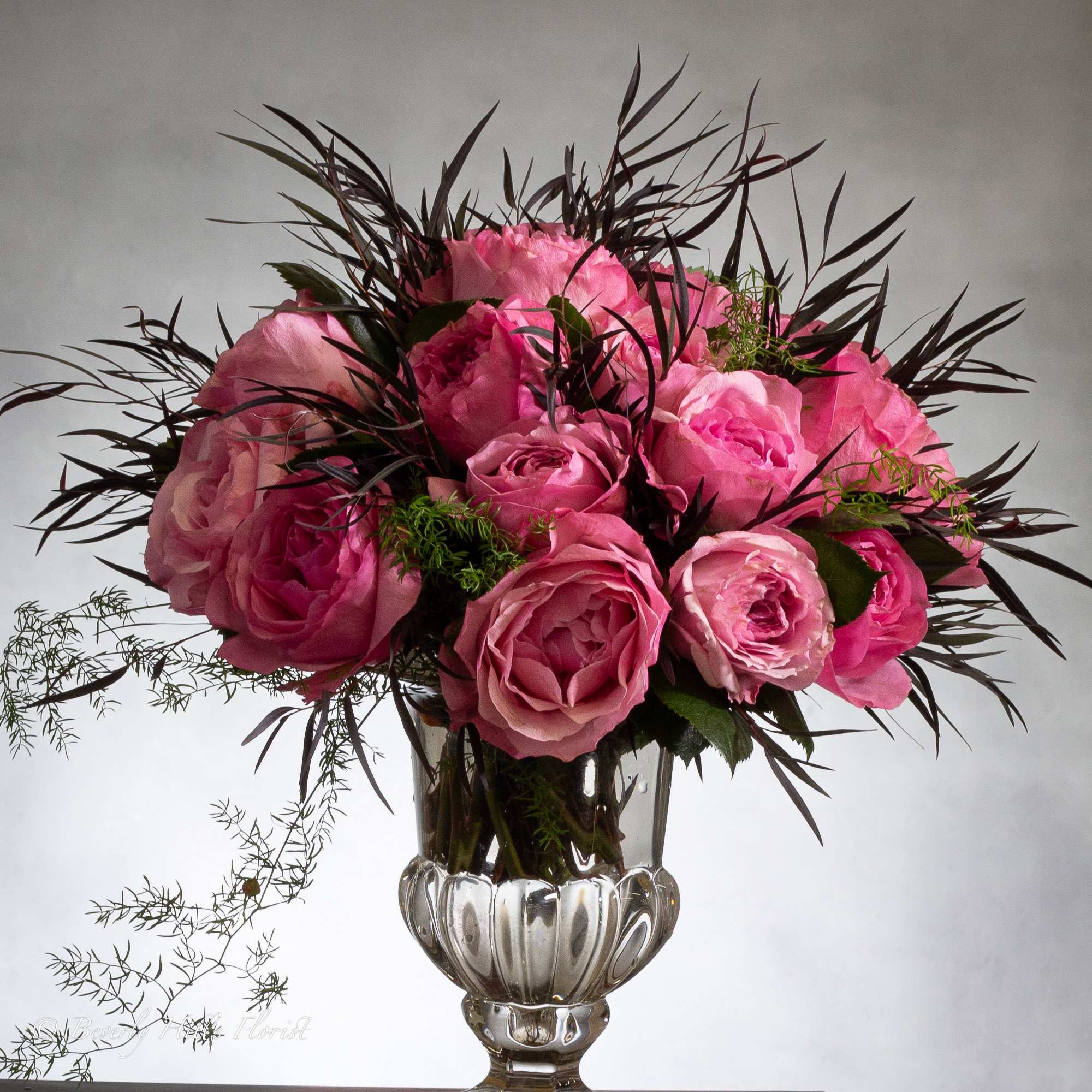 Luscious pink roses with seasonal floral and greens in leaf lined footed