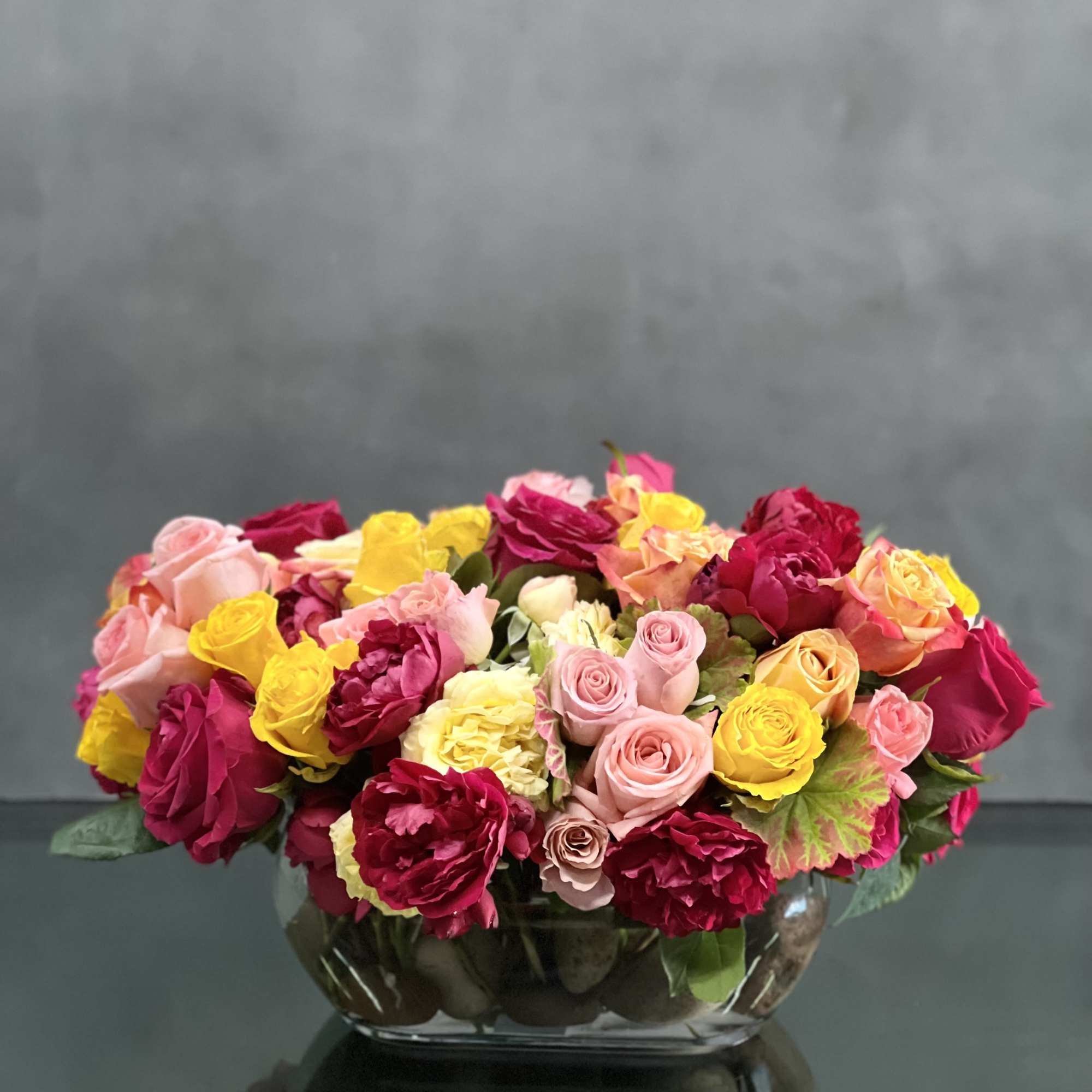 This arrangement of colorful roses  in an oval glass vase is