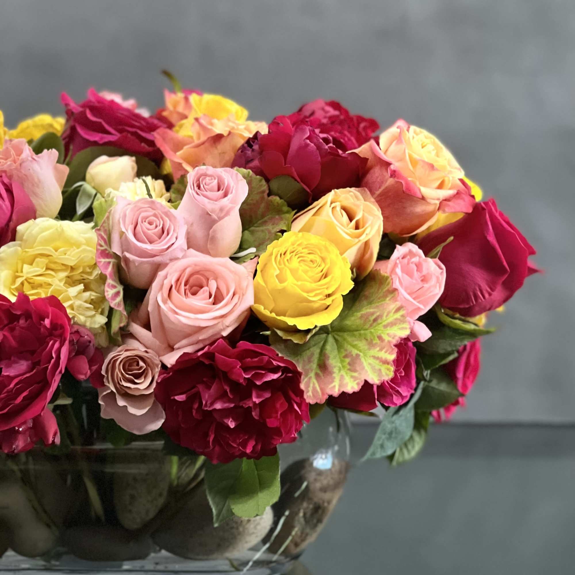 This arrangement of colorful roses  in an oval glass vase is