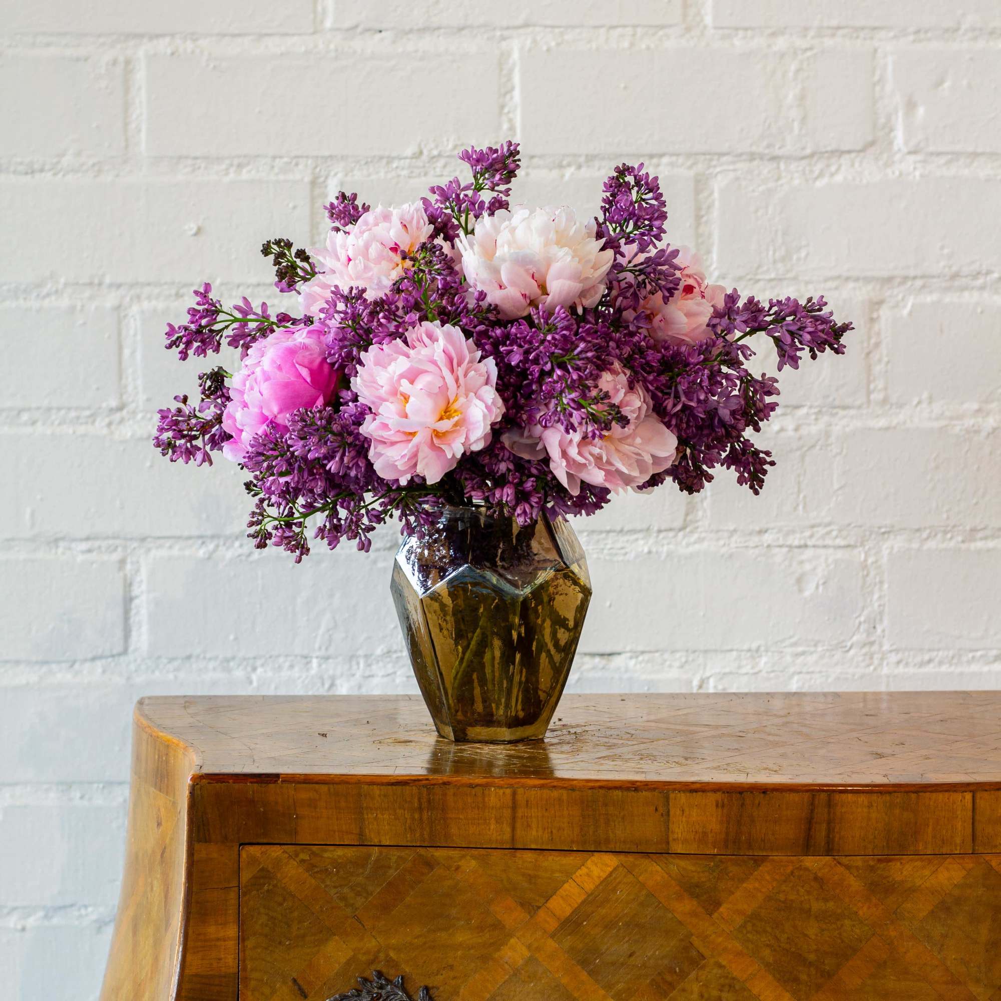 The beautiful arrangement features blush color peonies and purple lilacs gathered together