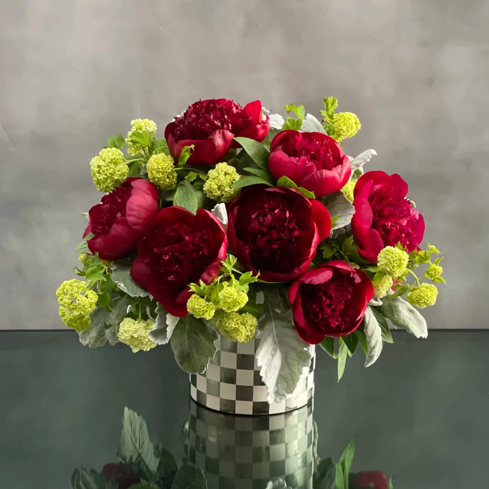 This arrangement includes rich burgundy peonies with green accents in a shiny