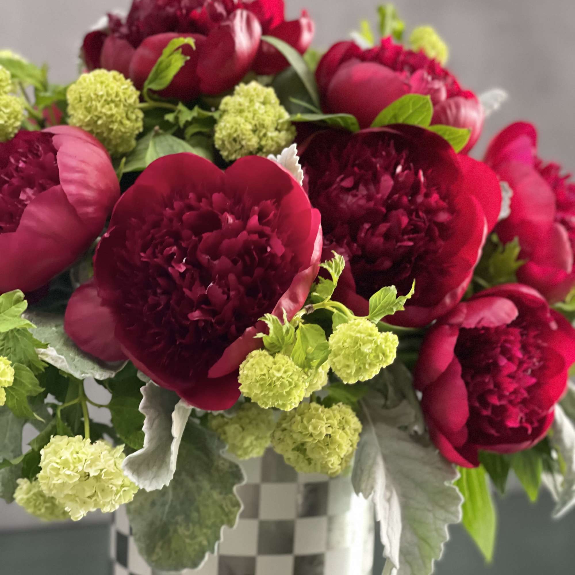 This arrangement includes rich burgundy peonies with green accents in a shiny
