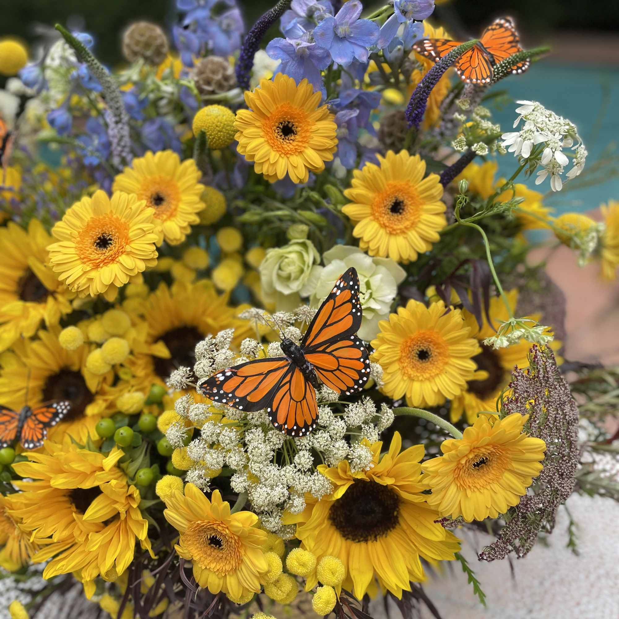 This magnificent arrangement combines vibrant sunflowers, delicate daisies, and elegant delphiniums. The