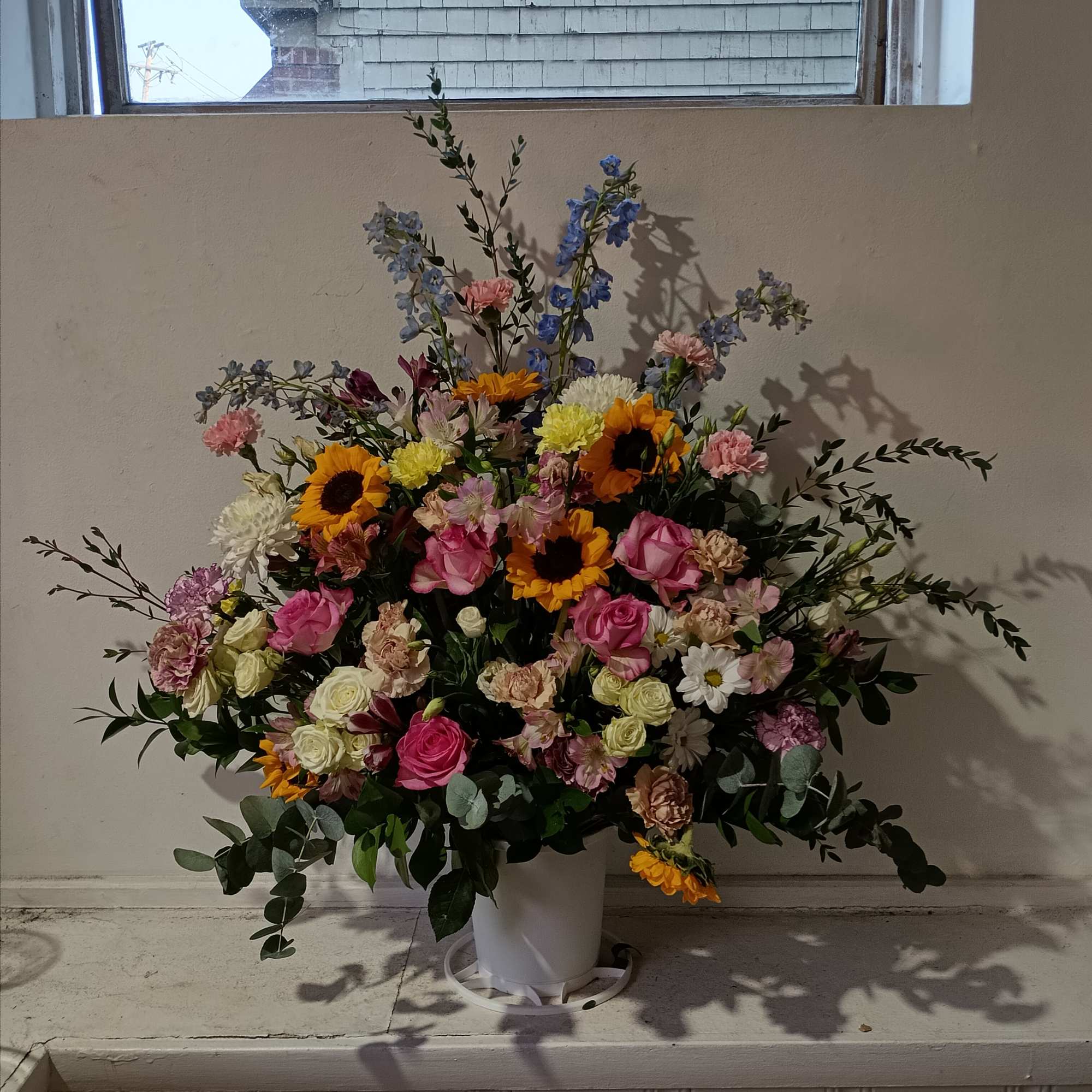 Beautiful sympathy basket with sunflowers, pale pink carnations, pink roses and delphinium
