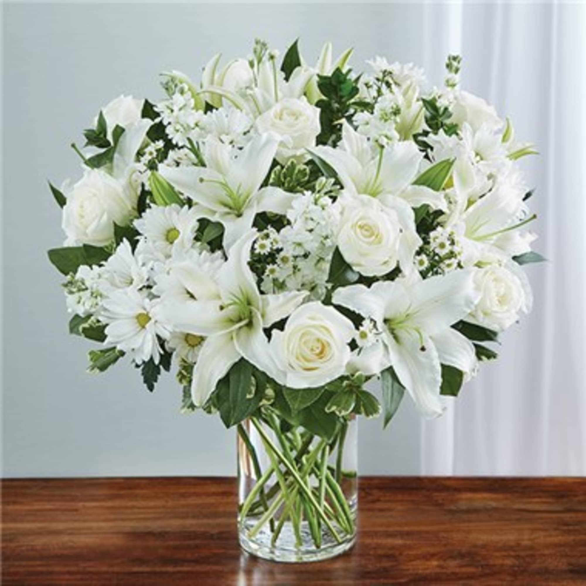 Express your sincere condolences with our elegant all-white arrangement of roses, lilies