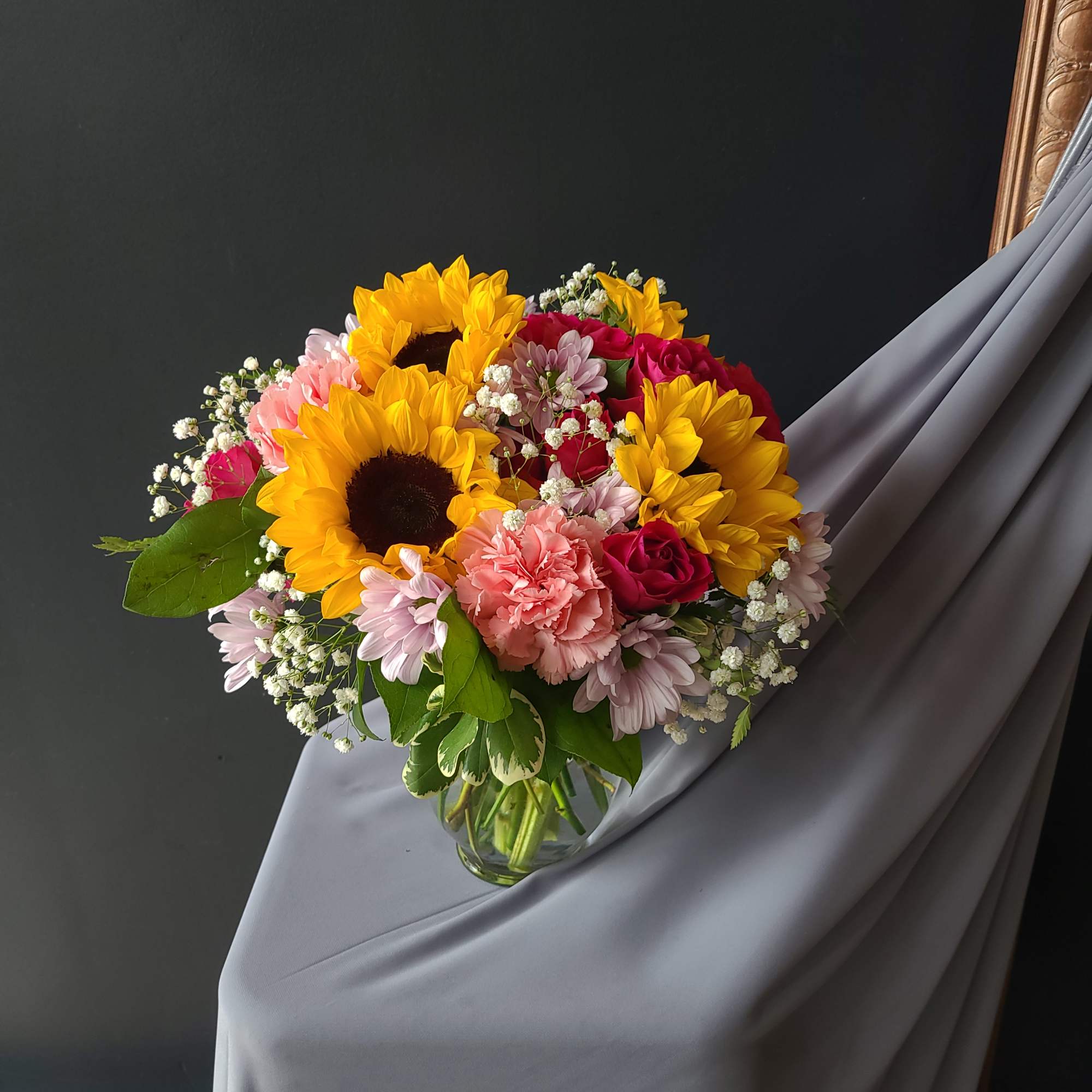 A delicate arrangement of sunflowers, daisies, and spray roses. Sweetly complimented with