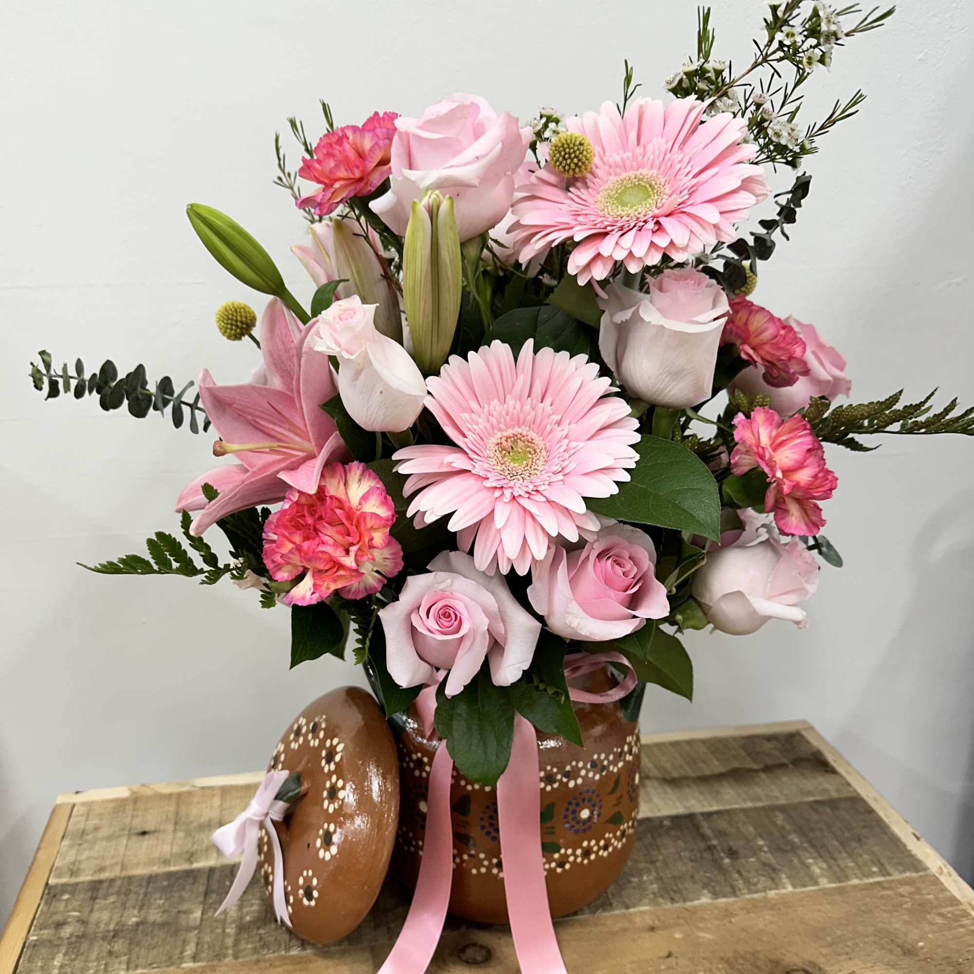A charming clay pot filled with light, pink roses, cheerful pink daisies