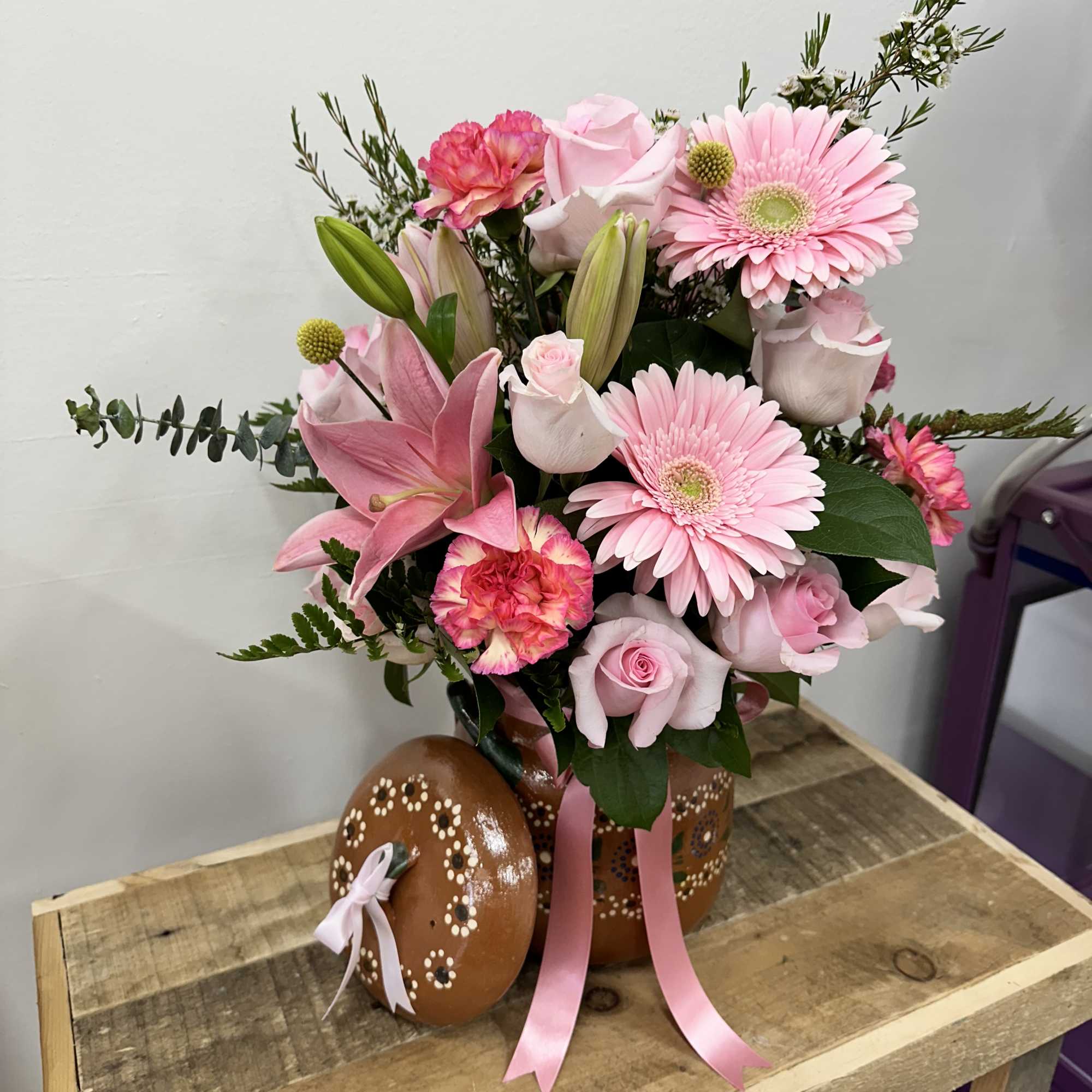 A charming clay pot filled with light, pink roses, cheerful pink daisies