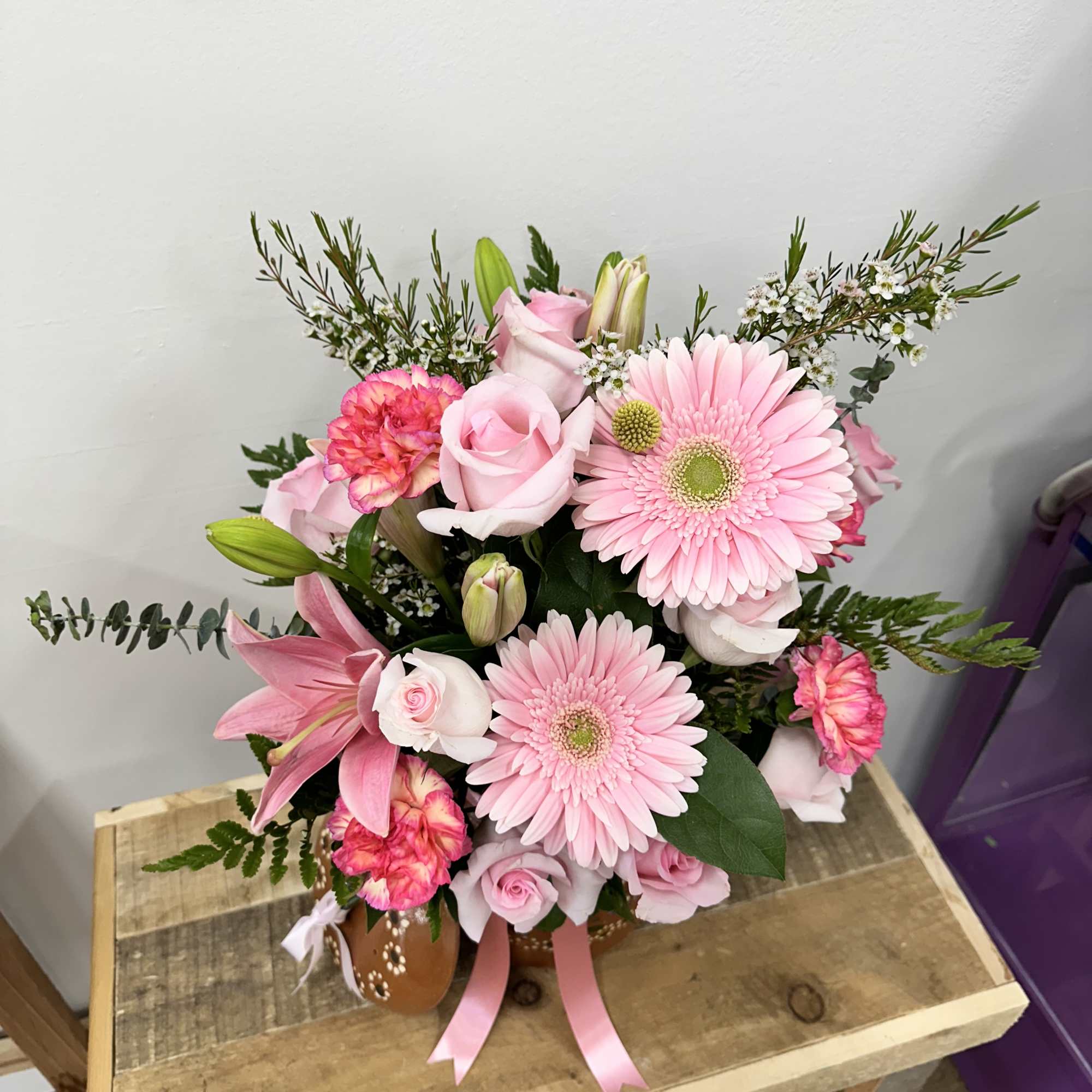A charming clay pot filled with light, pink roses, cheerful pink daisies