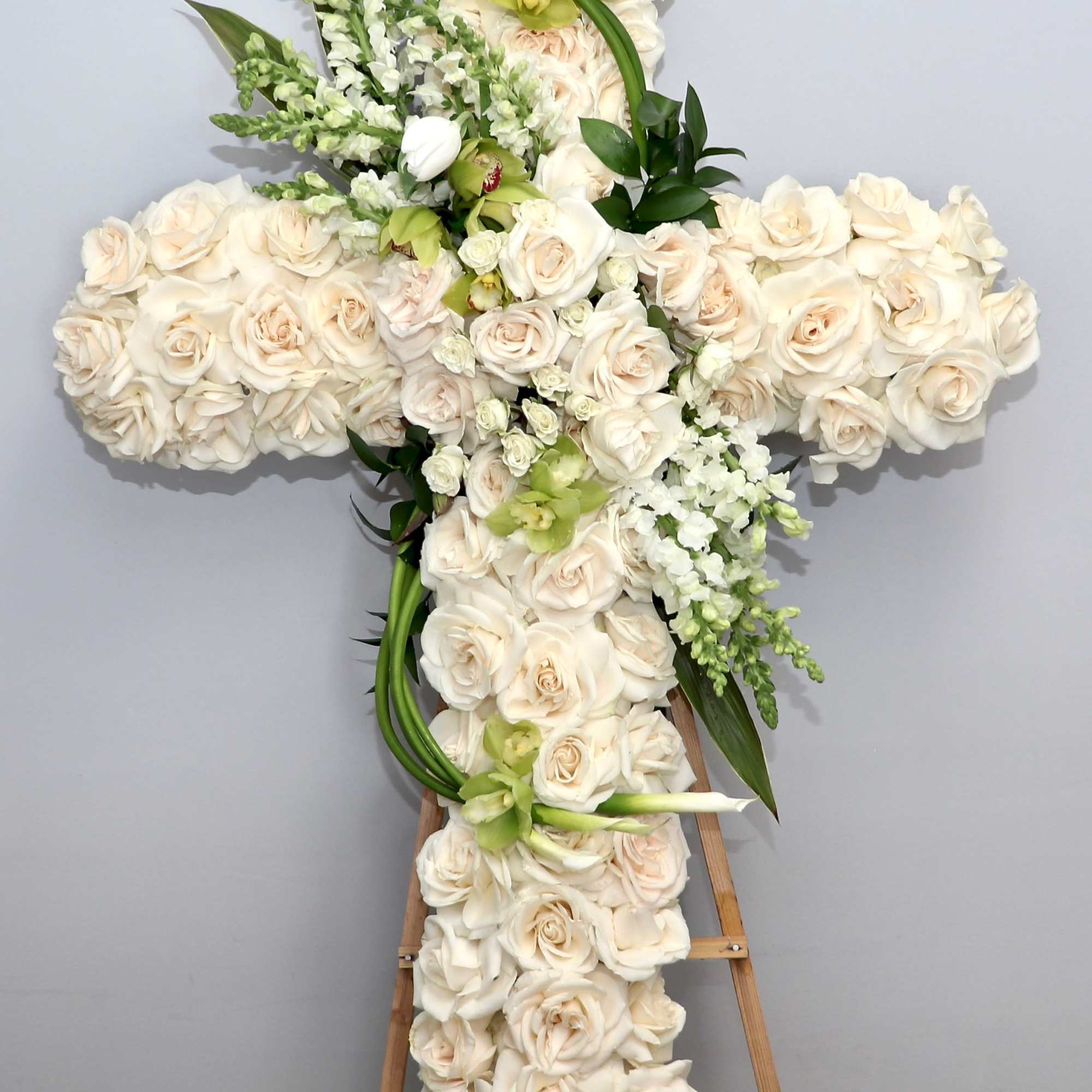 White Cross filled with roses, calla lilies and pop of green accents.

We