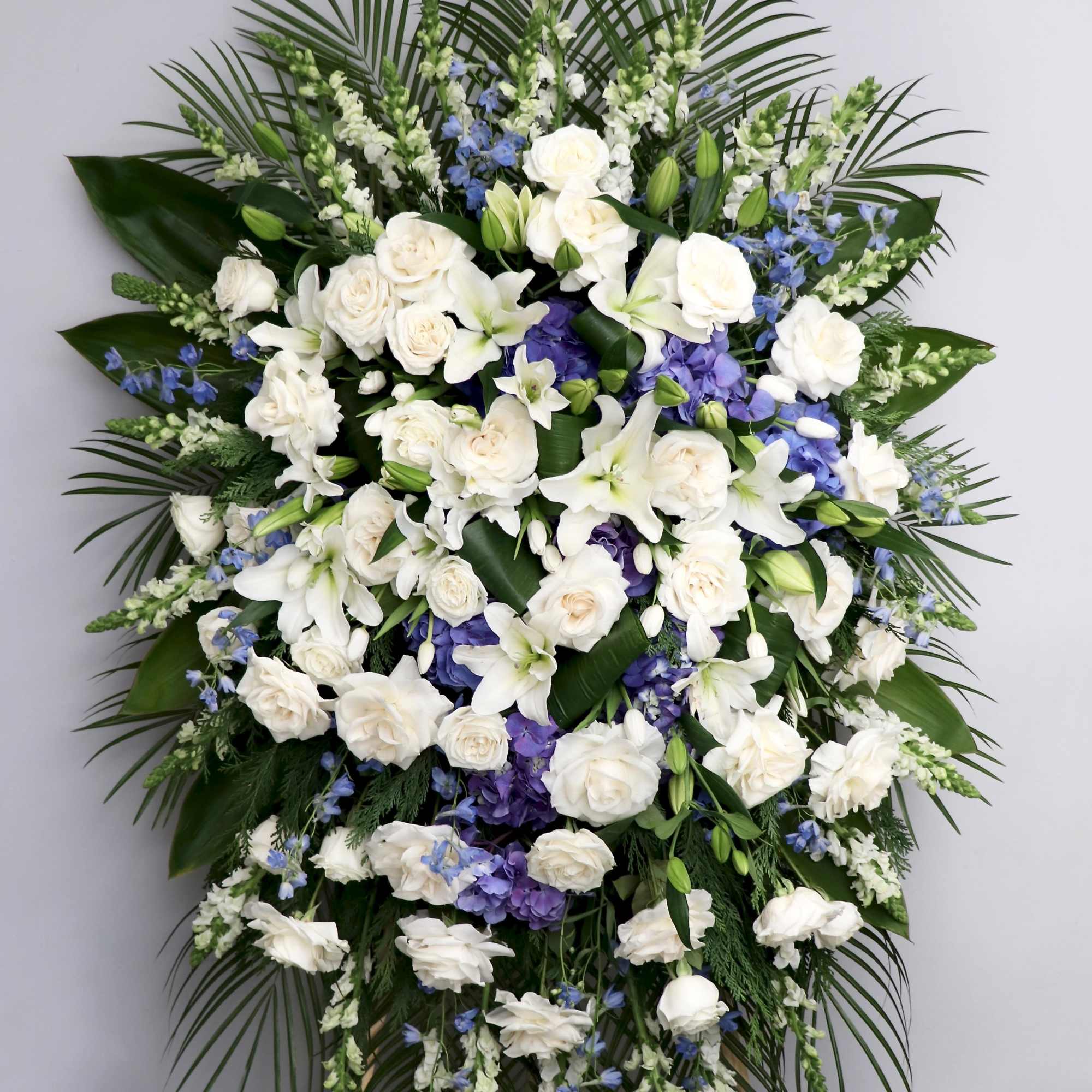 This spray is made with white roses and lilies with blue delphiniums
