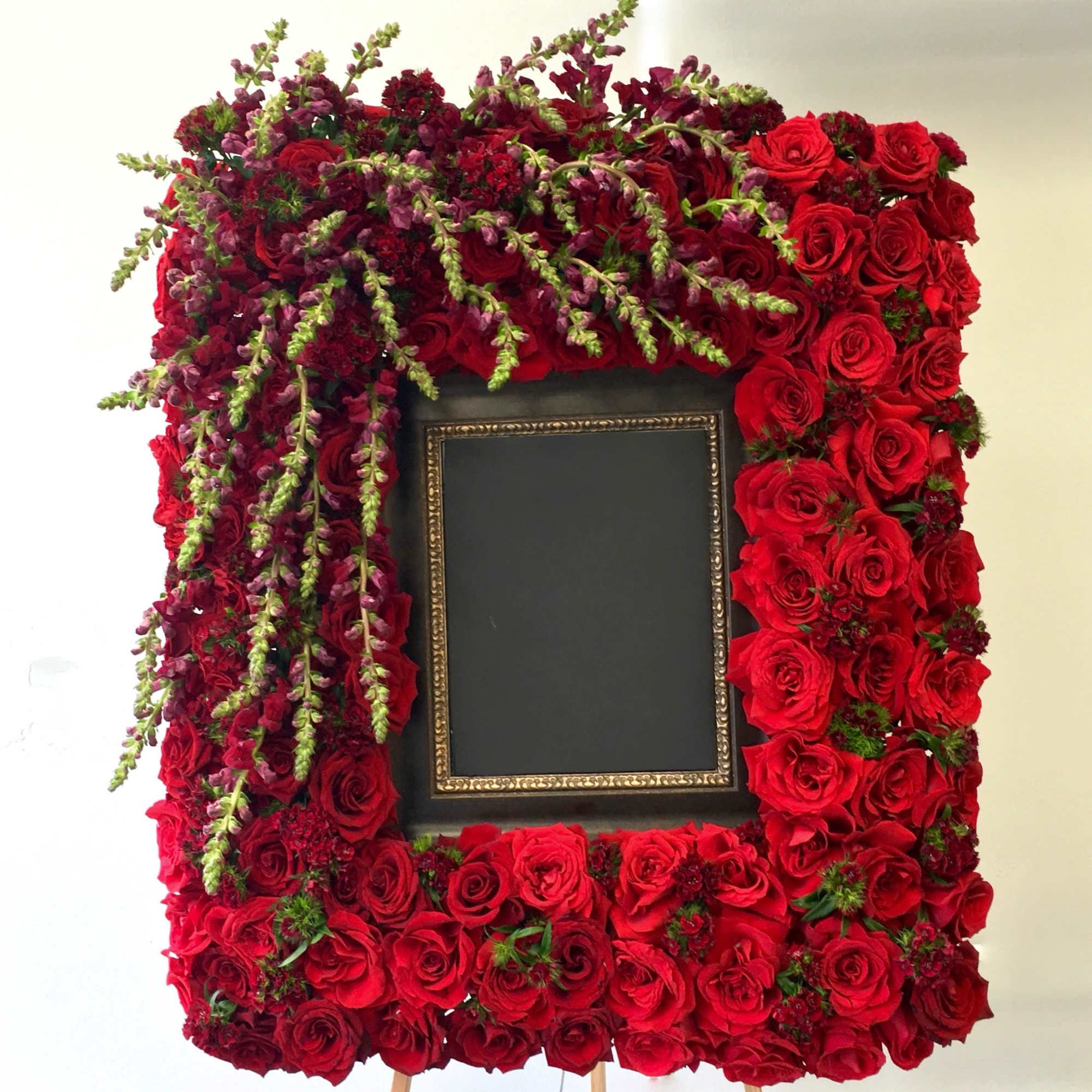 This frame includes red roses, snapdragons and dark seasonal greens. The standard