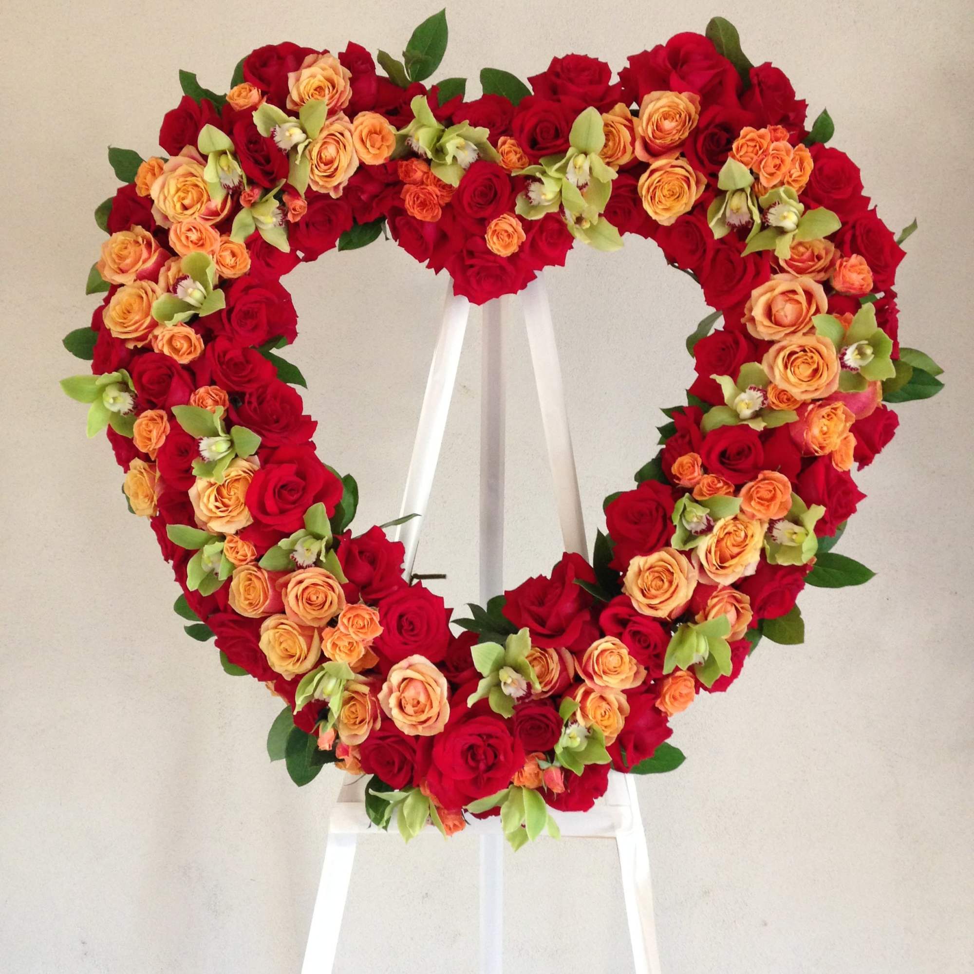 This heart contains red and orange roses, orchids, and minimal seasonal greens.