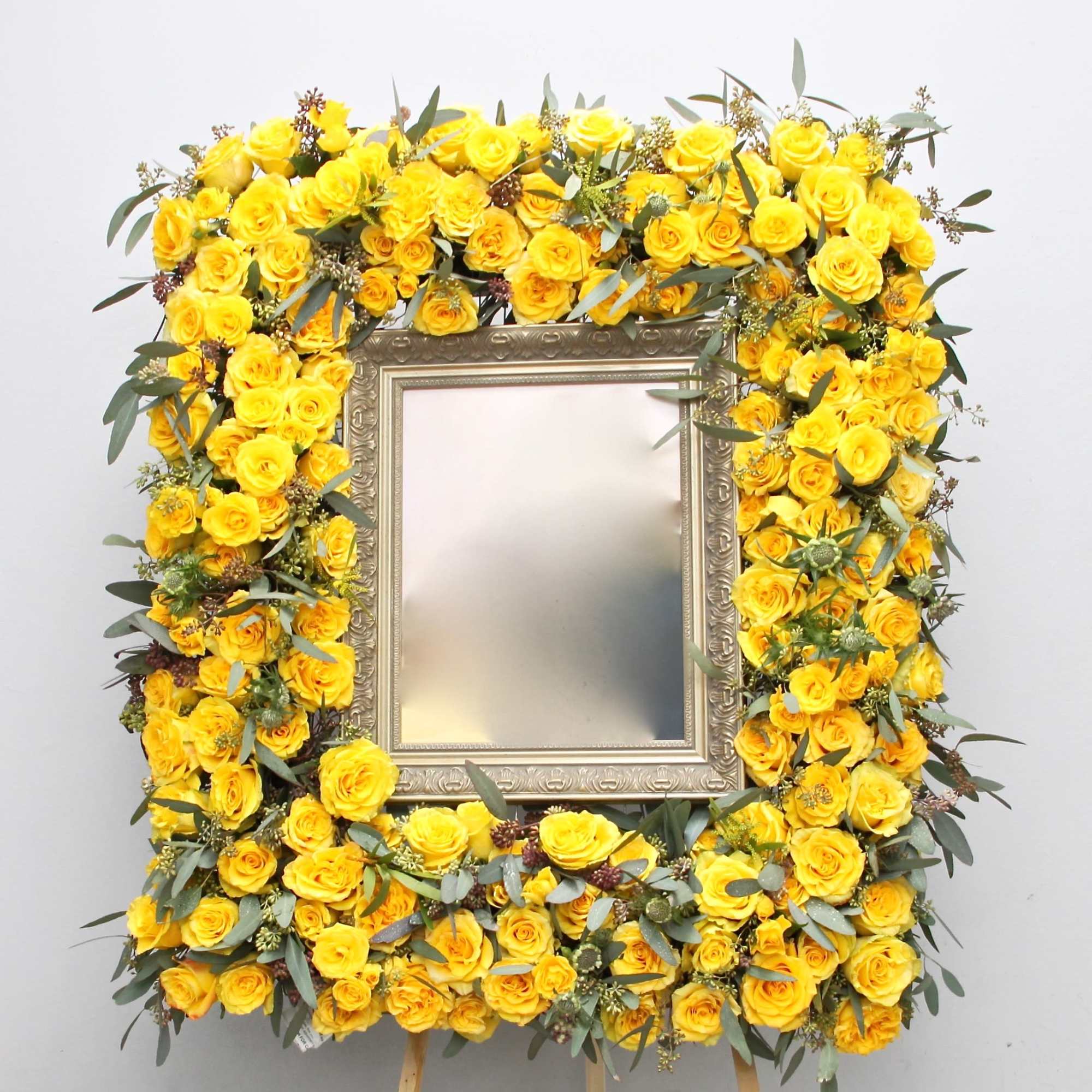 This frame is made up of bright yellow roses and seasonal greens.