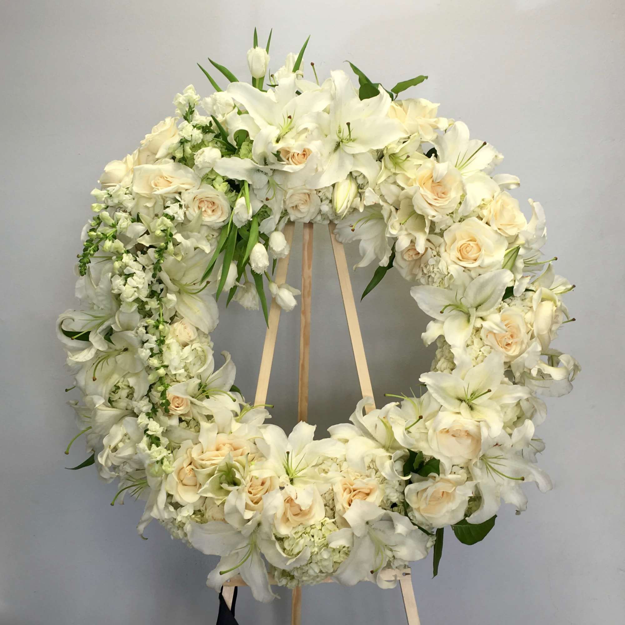 This wreath includes bright white stargazer lilies, roses, and seasonal greens. 
First