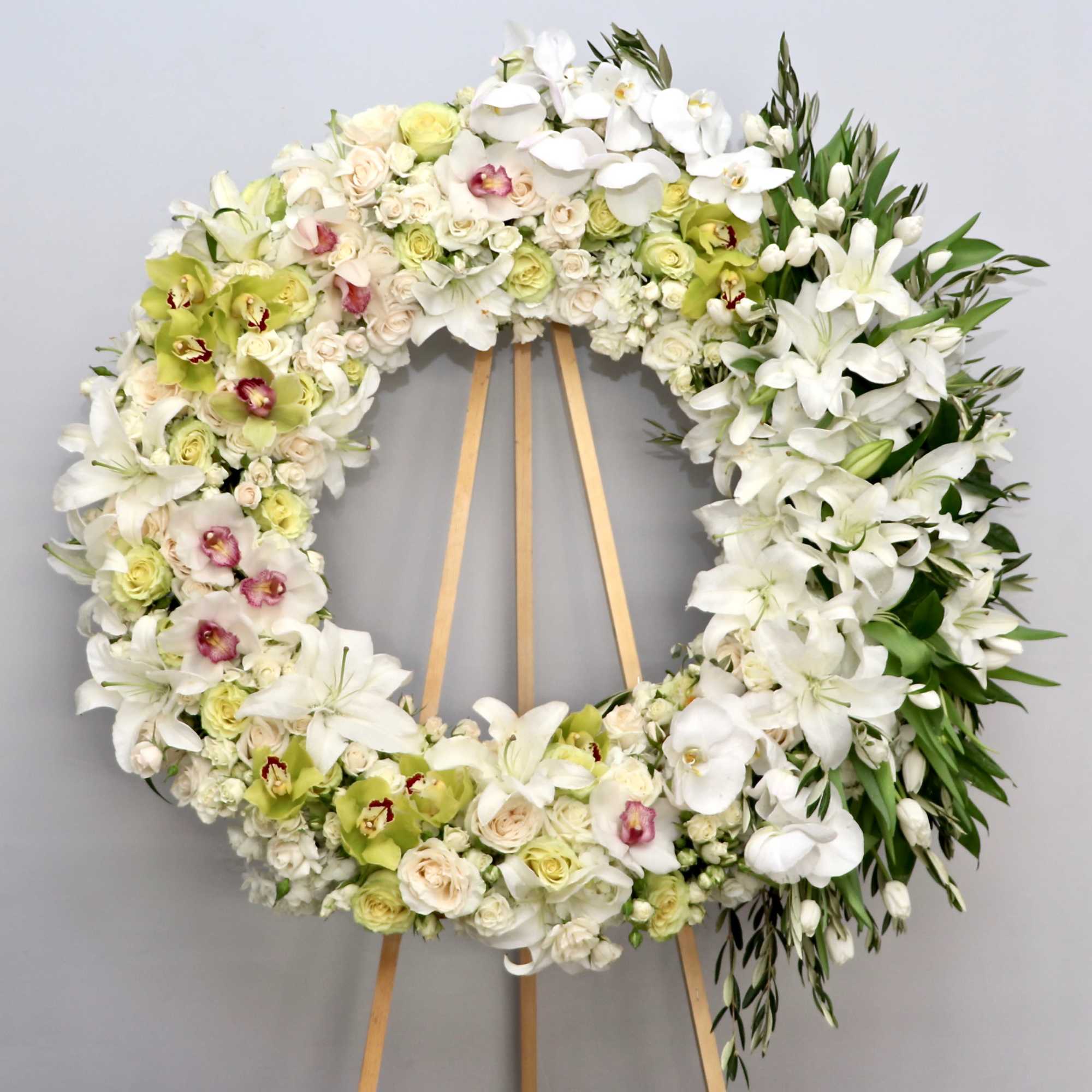 This wreath includes bright white stargazer lilies, roses, and seasonal greens. 
First