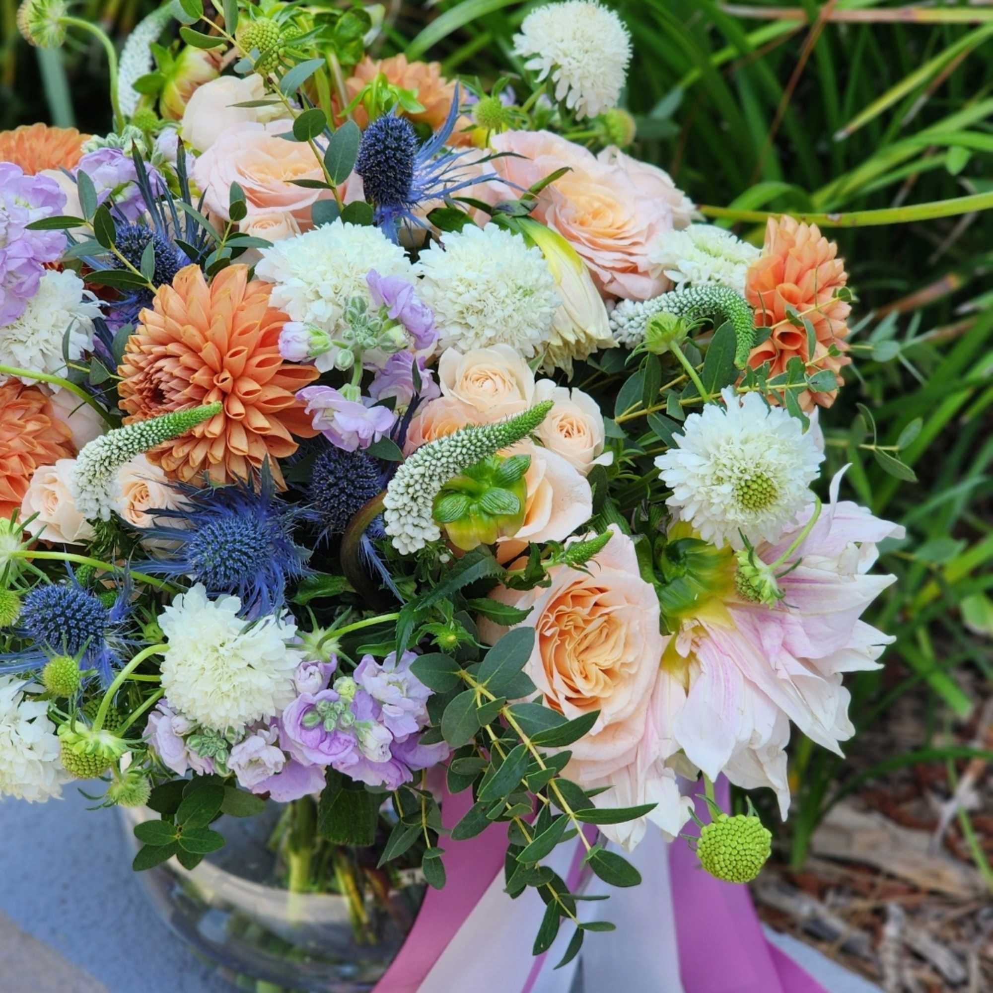  A clear vase arrangement featuring peach roses, vibrant orange dahlias, and