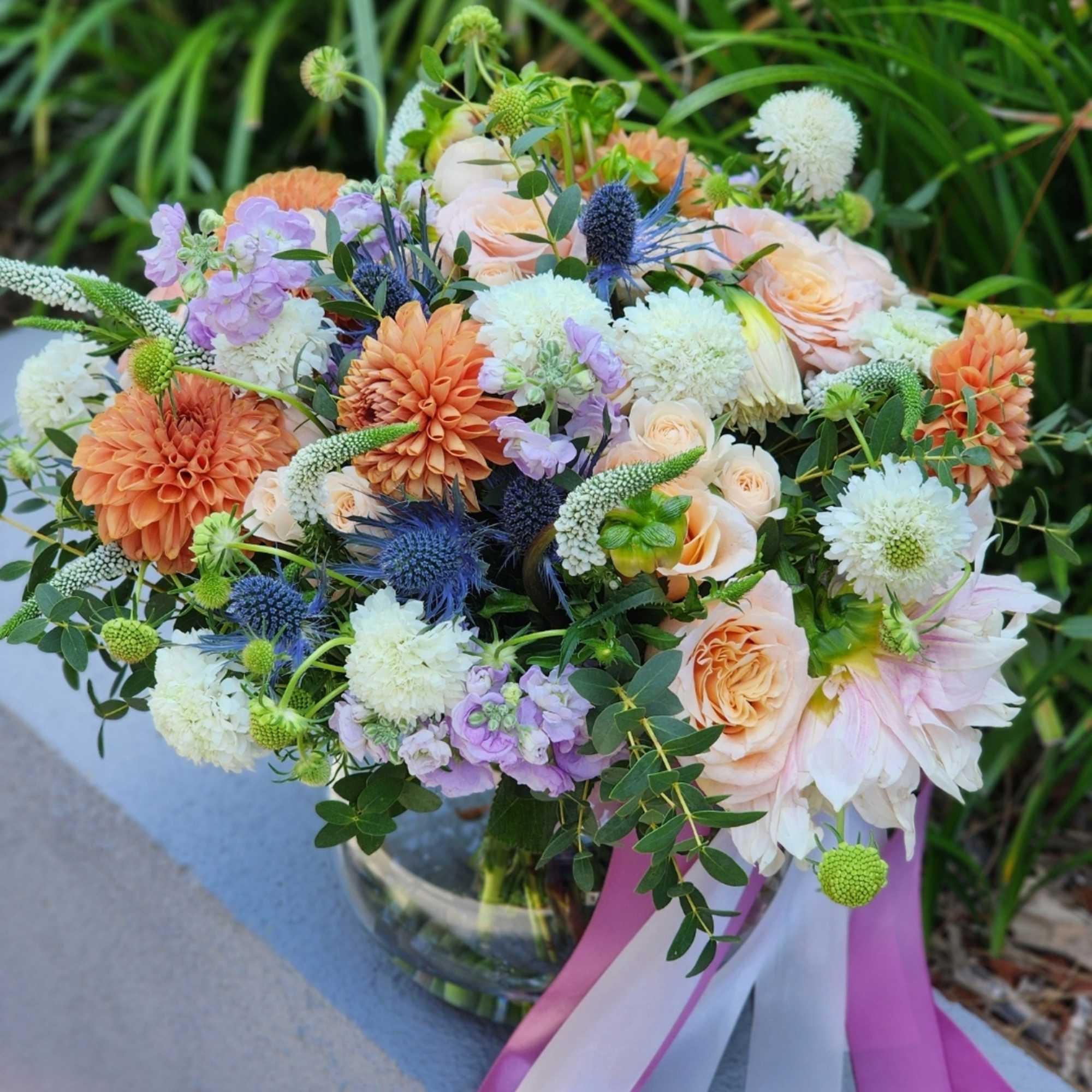  A clear vase arrangement featuring peach roses, vibrant orange dahlias, and