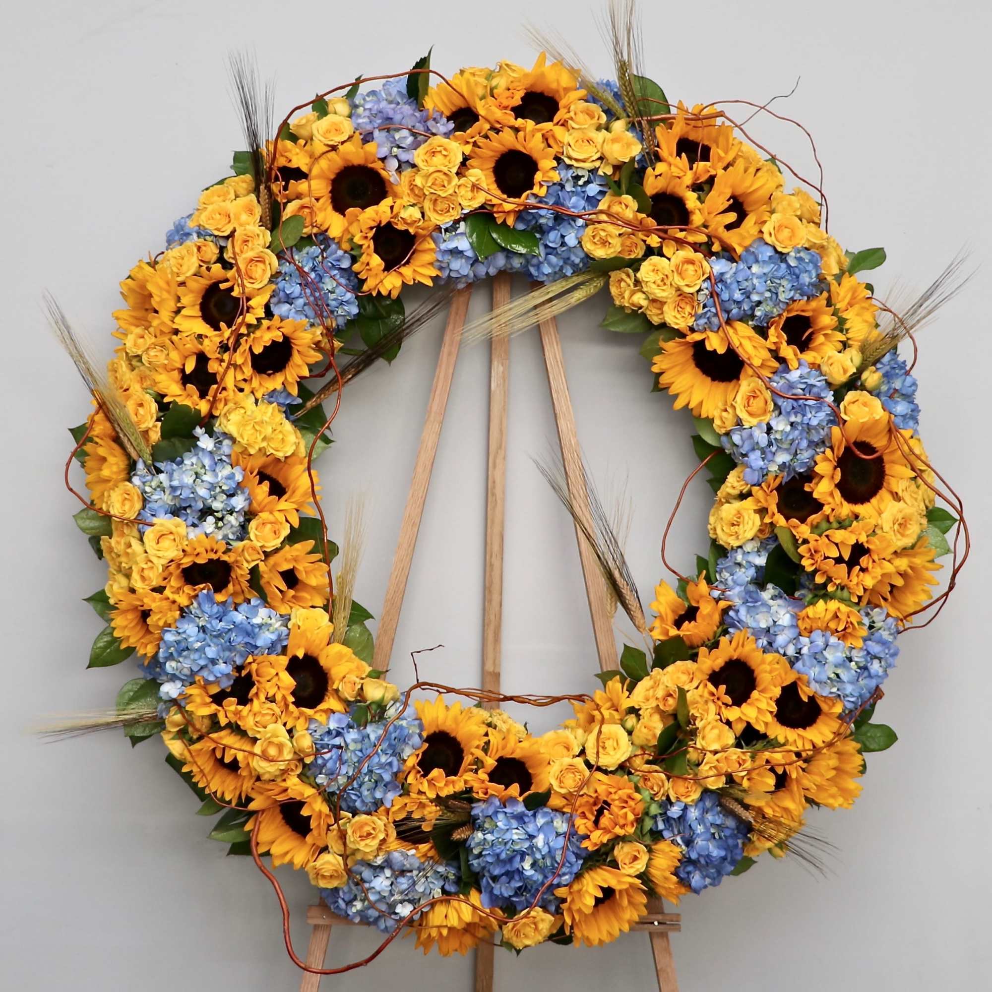 This sympathy wreath combines bright yellow sunflowers and roses with hydrangeas and