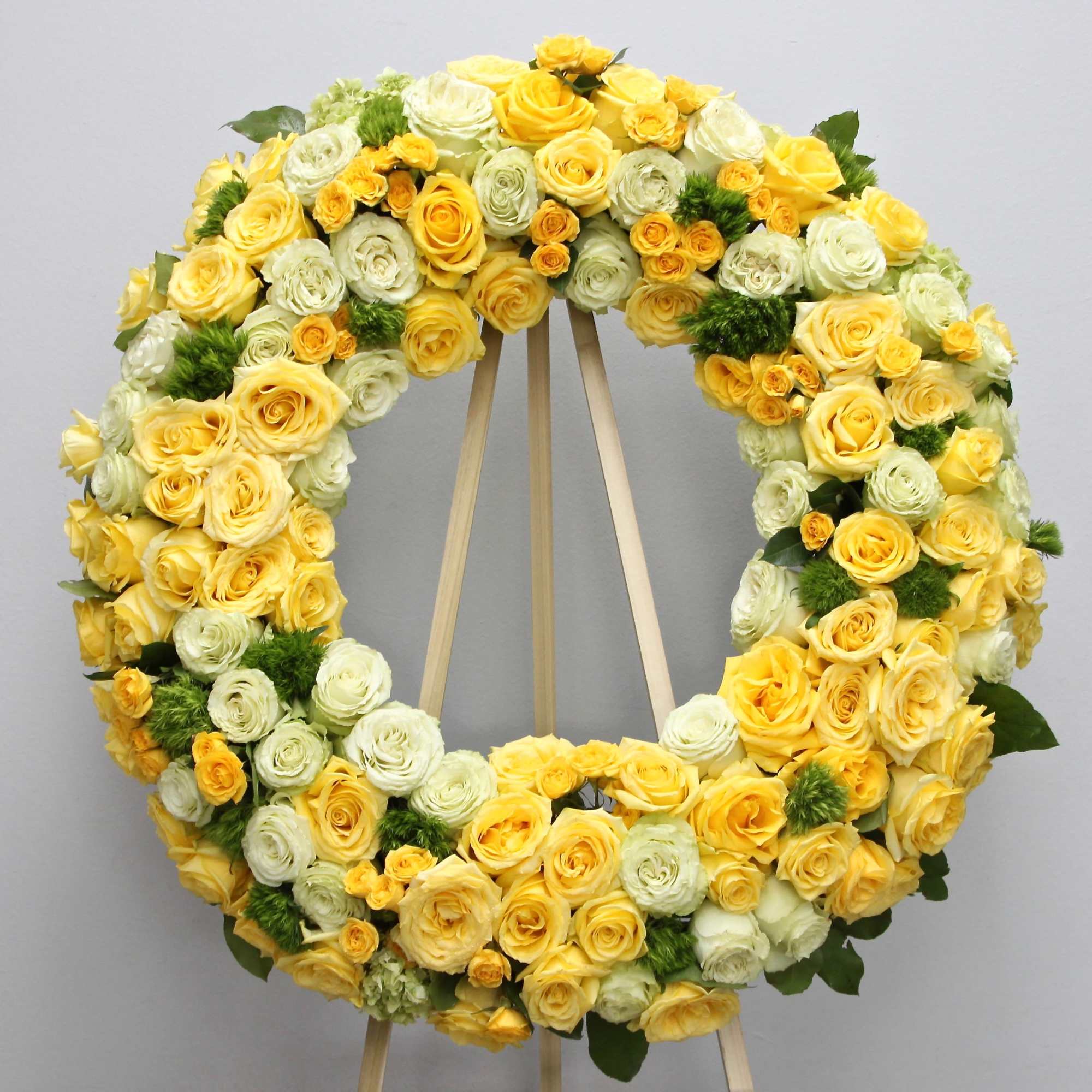 This sympathy spray includes bright yellow roses, hydrangeas, and fluffy seasonal greens.