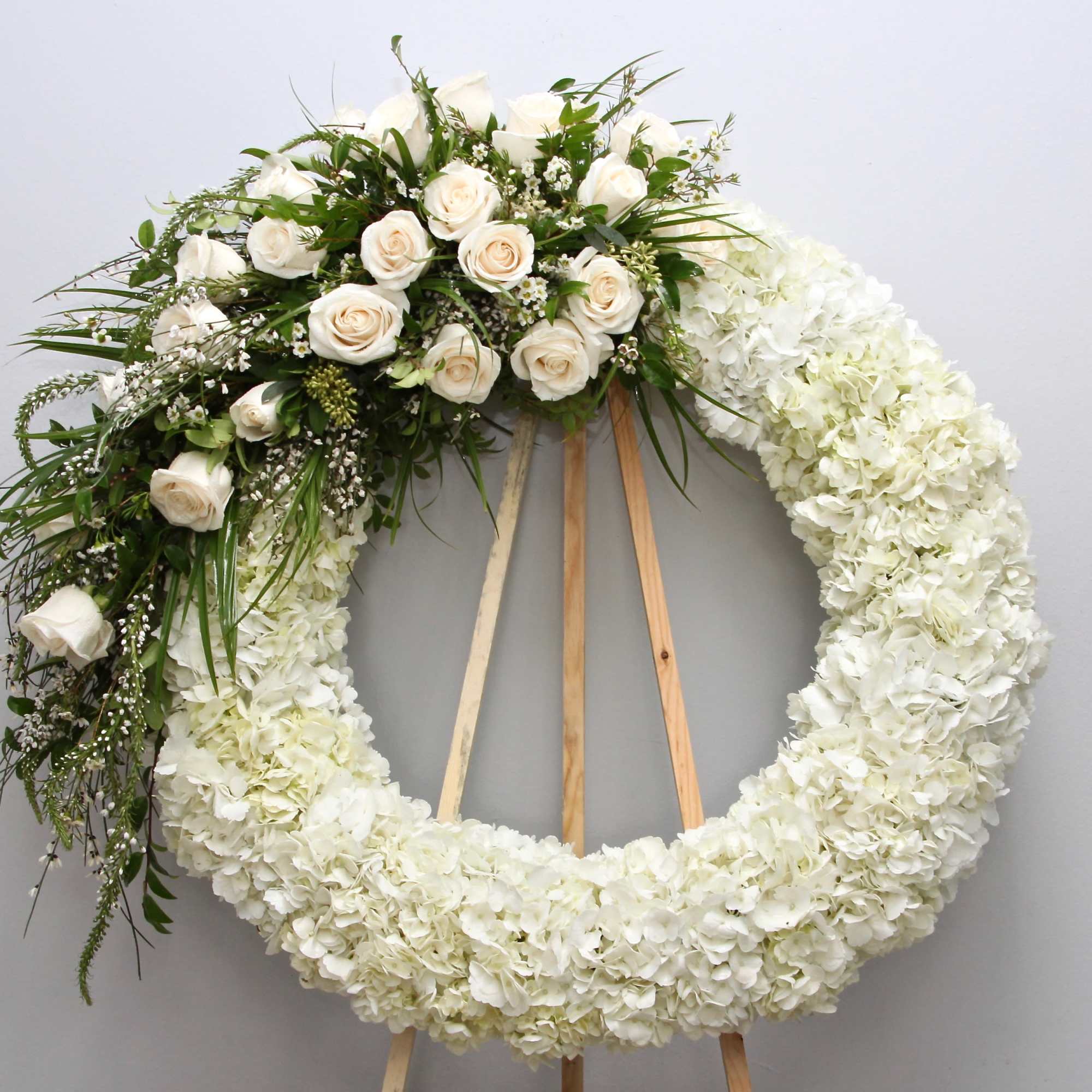 Textured with fluffy seasonal flowers, this wreath contains roses, hydrangeas, and fragrant