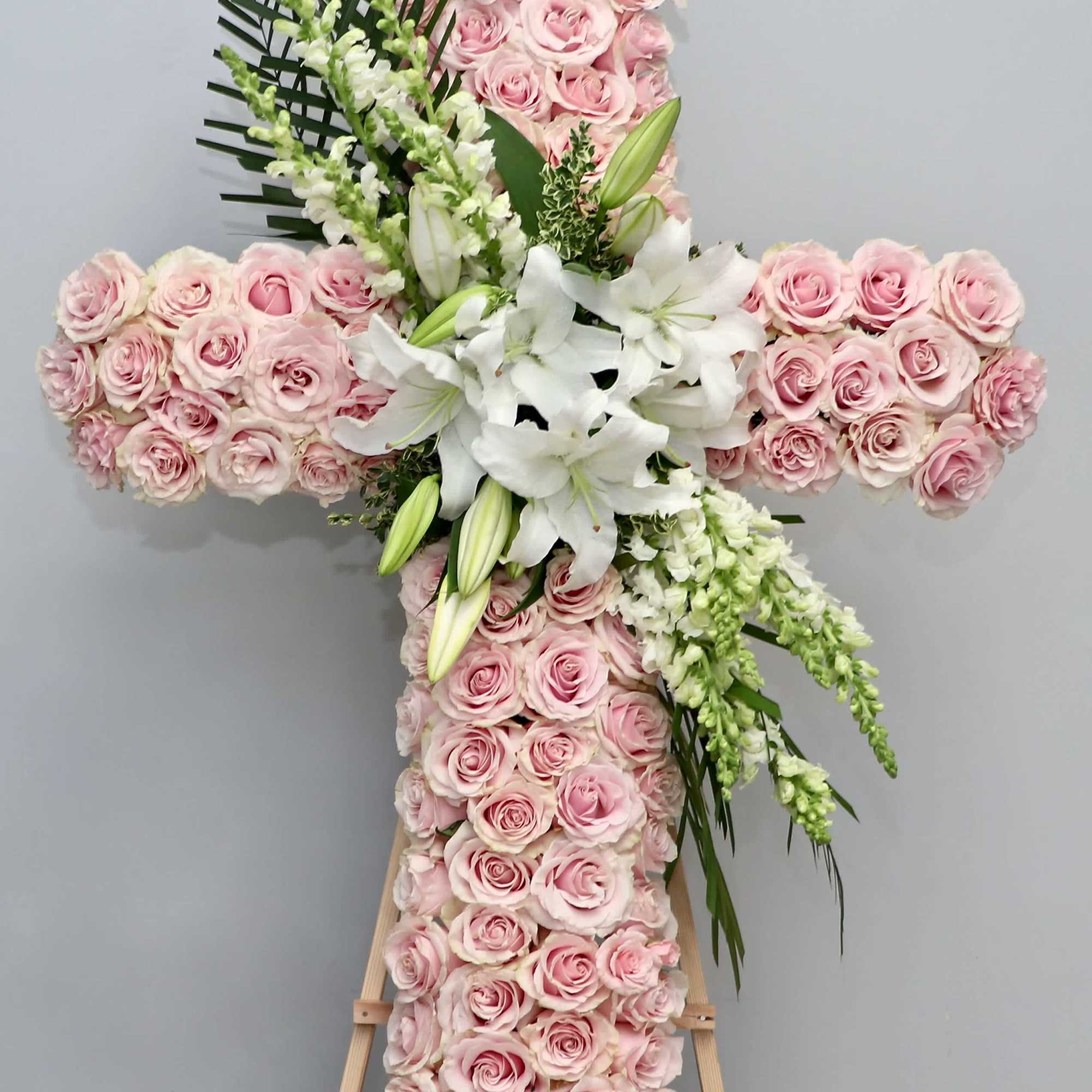This beautiful sympathy cross is carefully arranged with pink roses, snapdragons, and
