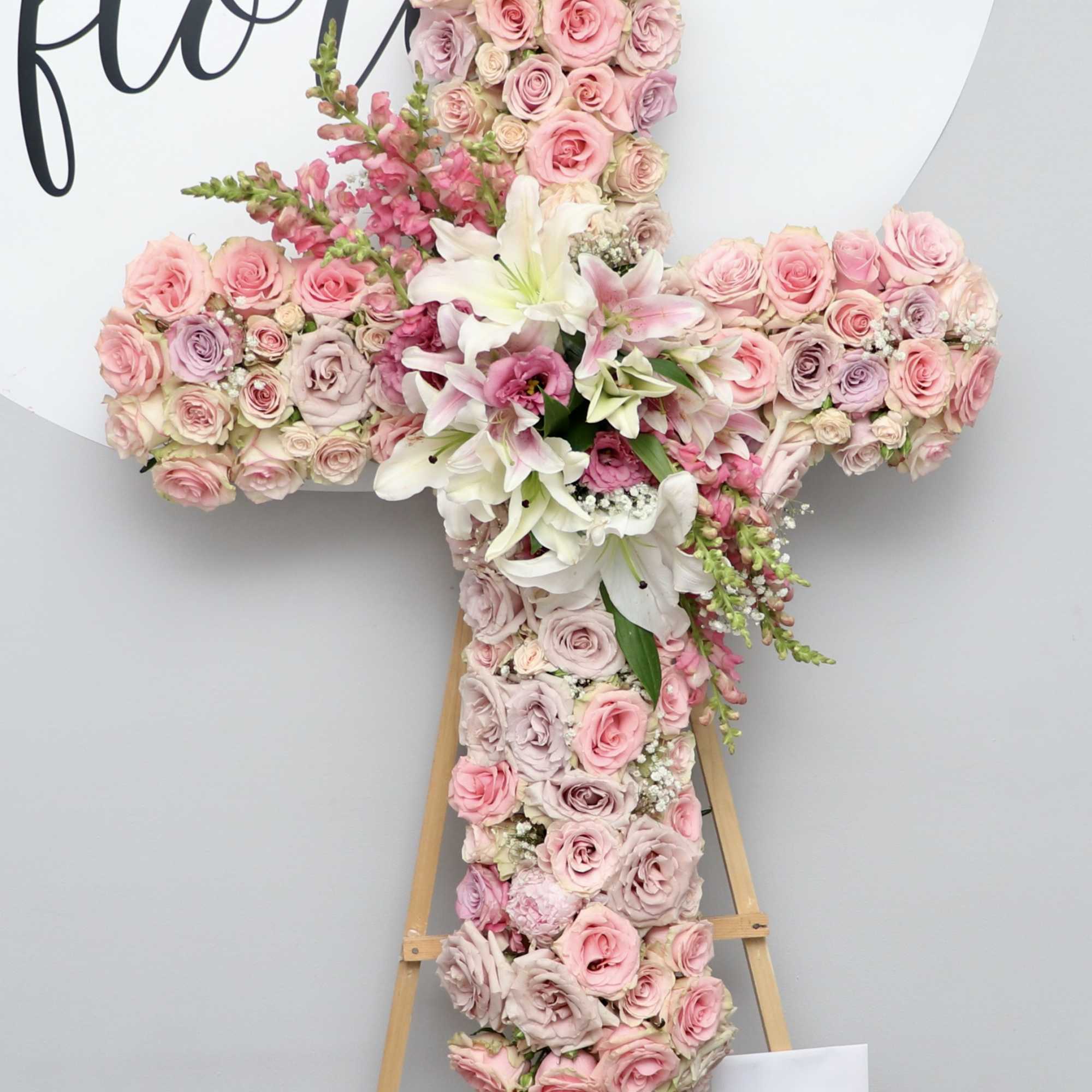 This beautiful sympathy cross is carefully arranged with pink roses, snapdragons, and