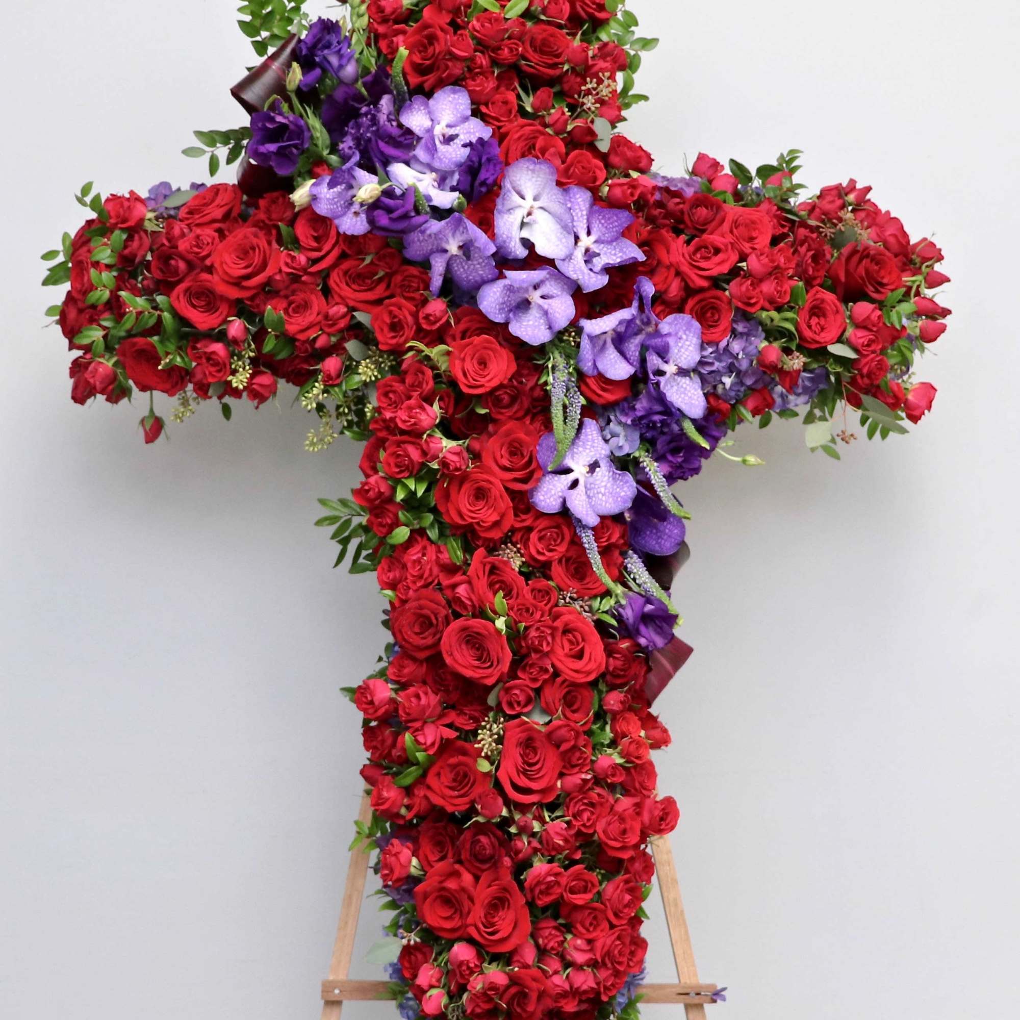 This sympathy cross contains vibrant red roses and purple orchids with touches