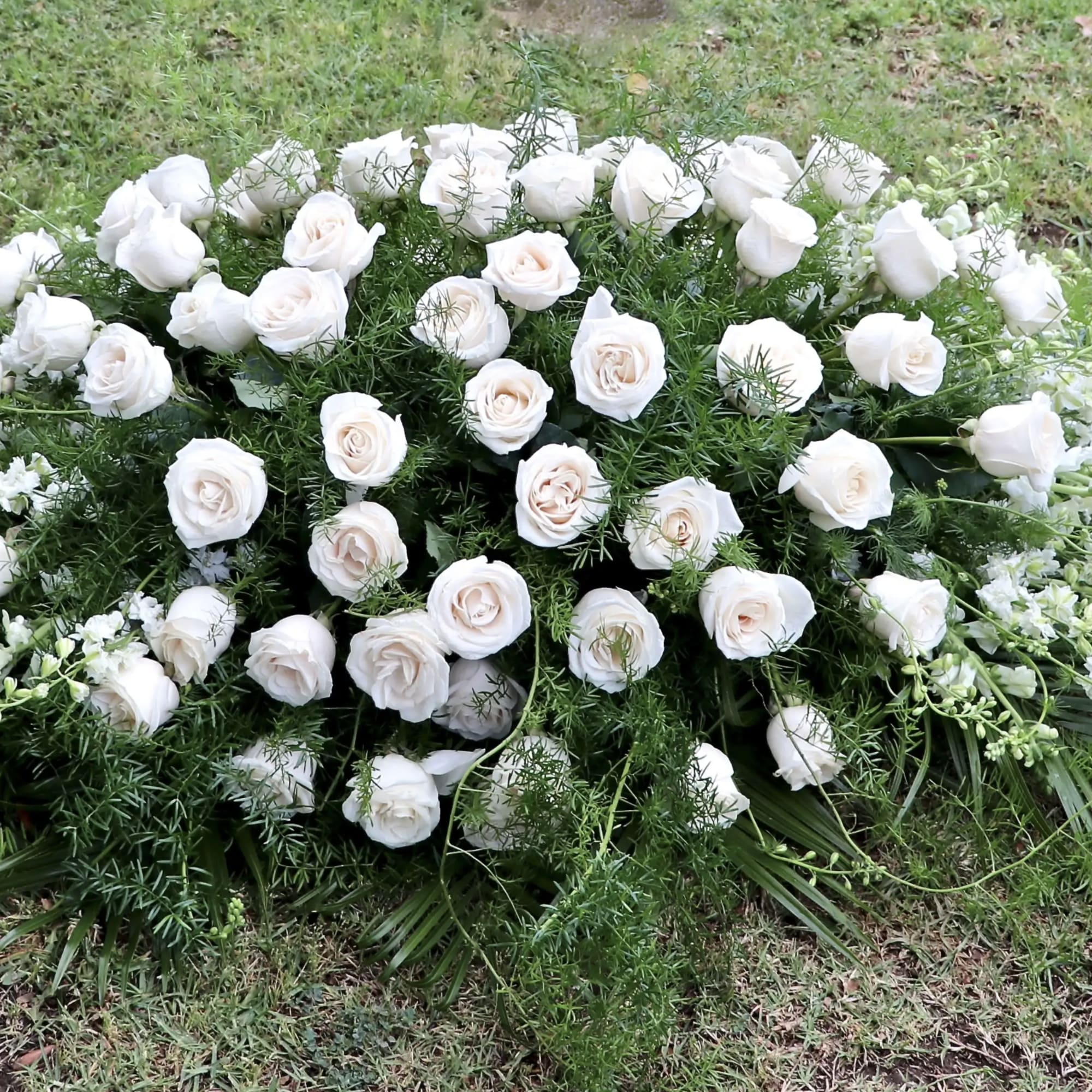 This casket spray includes white roses, snapdragons, and fragrant greens. 

Standard size