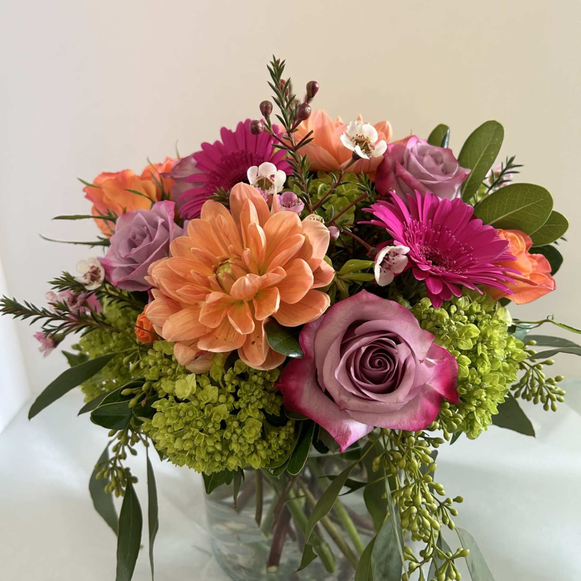 An Vase Arrangment with beautiful purple roses, Orange Dahlias and spray roses An Vase Arrangment with beautiful purple roses, Orange Dahlias and spray roses