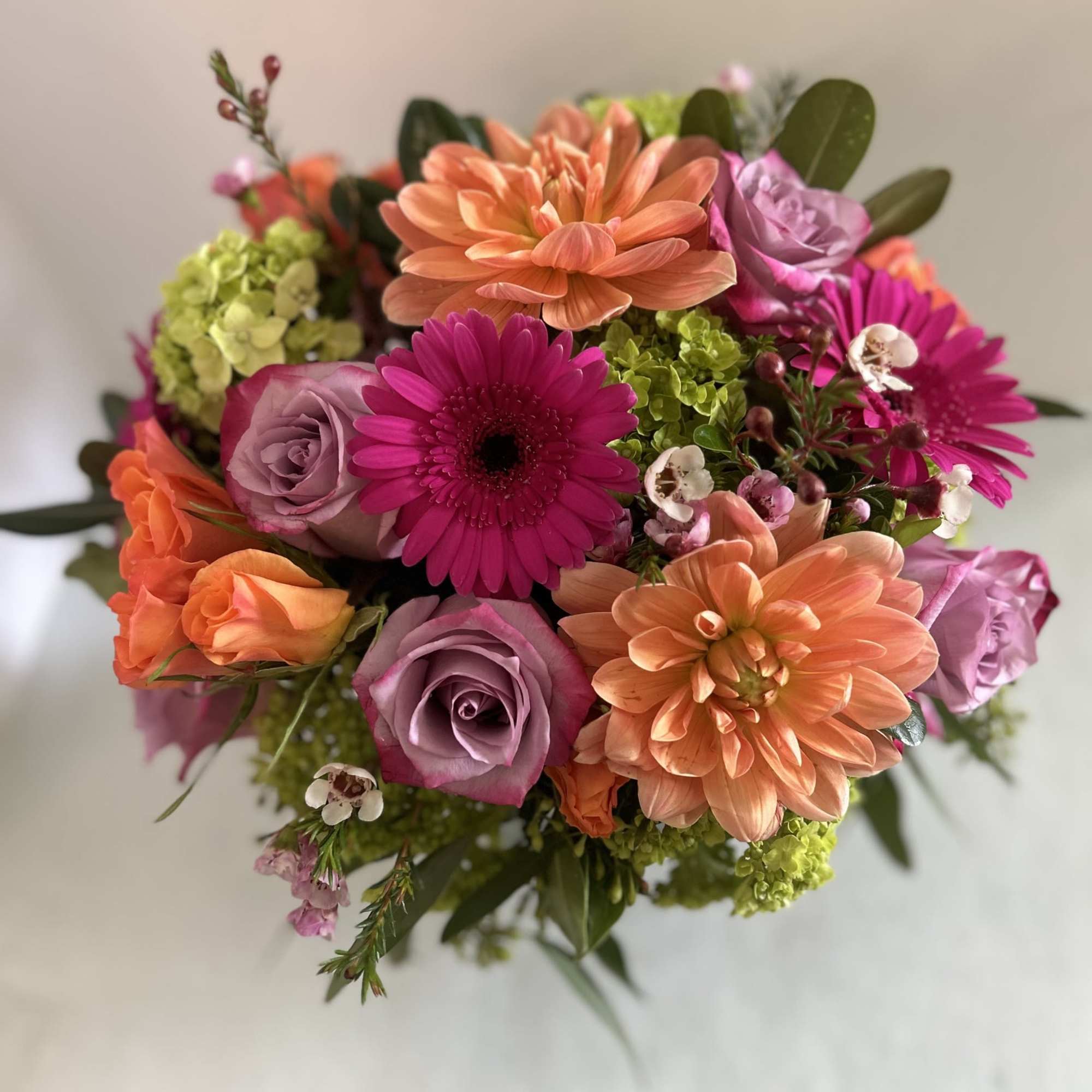 An Vase Arrangment with beautiful purple roses, Orange Dahlias and spray roses An Vase Arrangment with beautiful purple roses, Orange Dahlias and spray roses