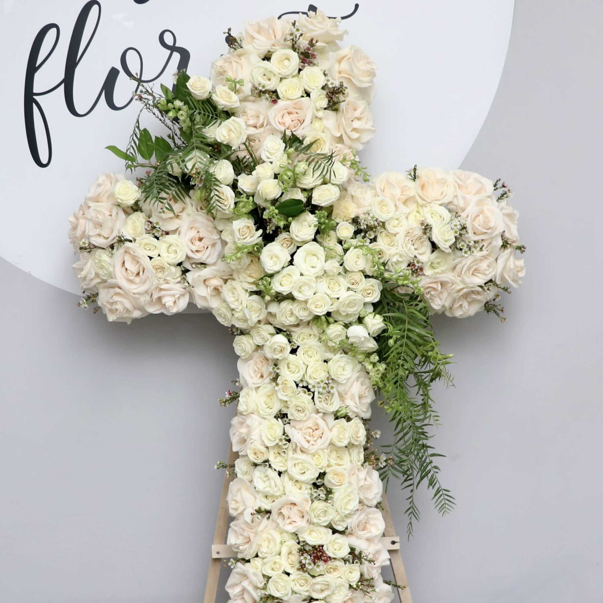 White Cross filled with roses, spray roses and pop of green accents.

We