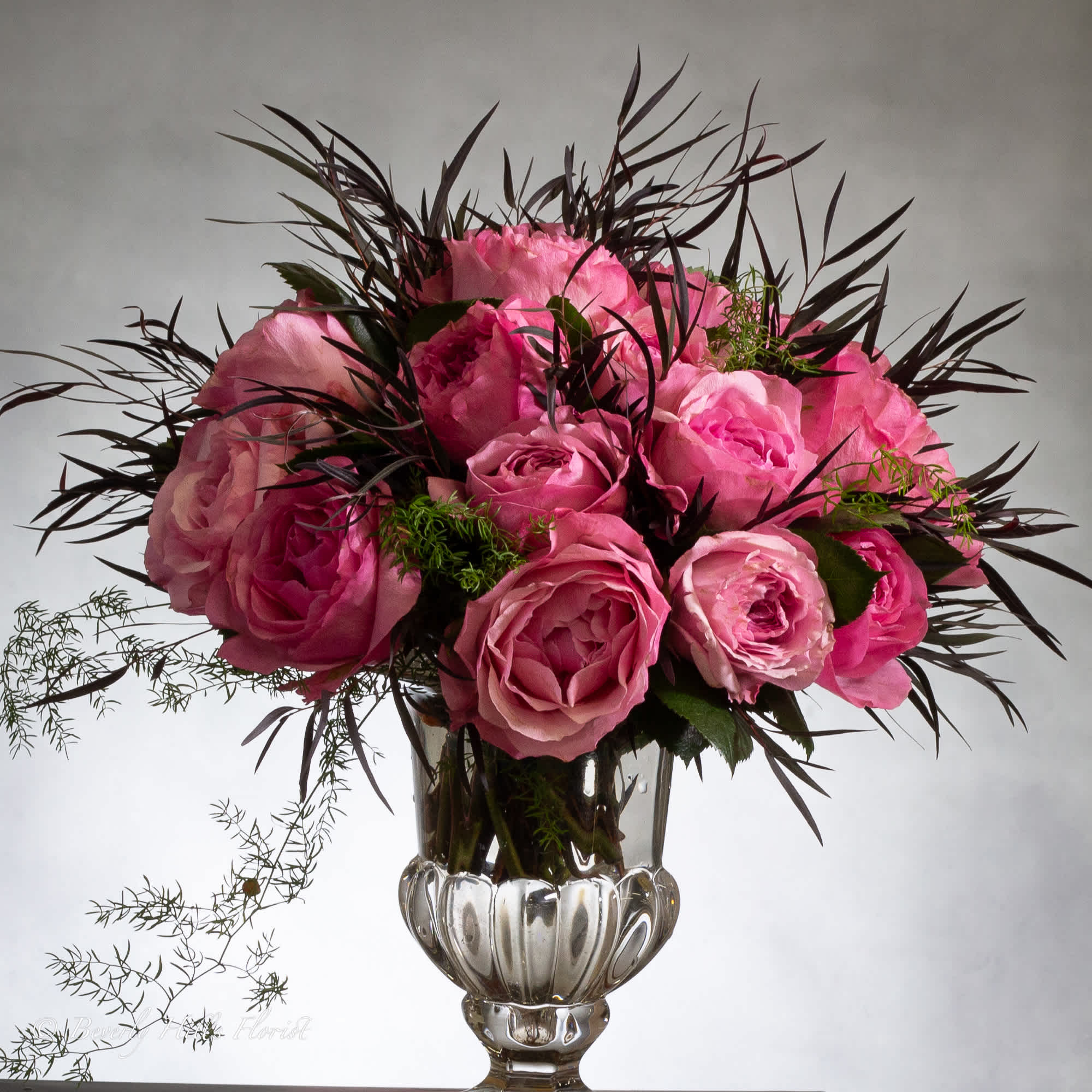 Luscious pink roses with seasonal floral and greens in leaf lined footed Luscious pink roses with seasonal floral and greens in leaf lined footed