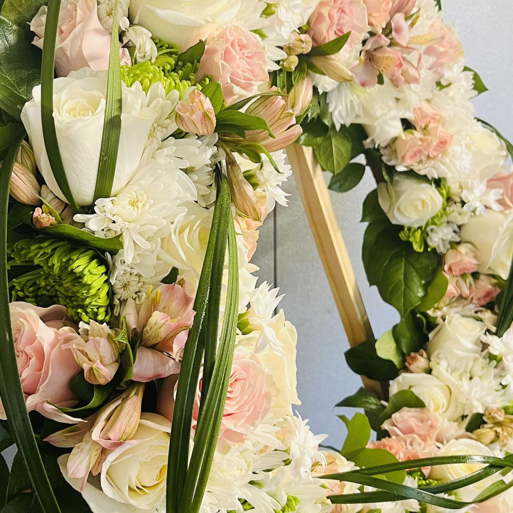 This gentle Tribute wreath using, soft whites, pinks and spring greens, is