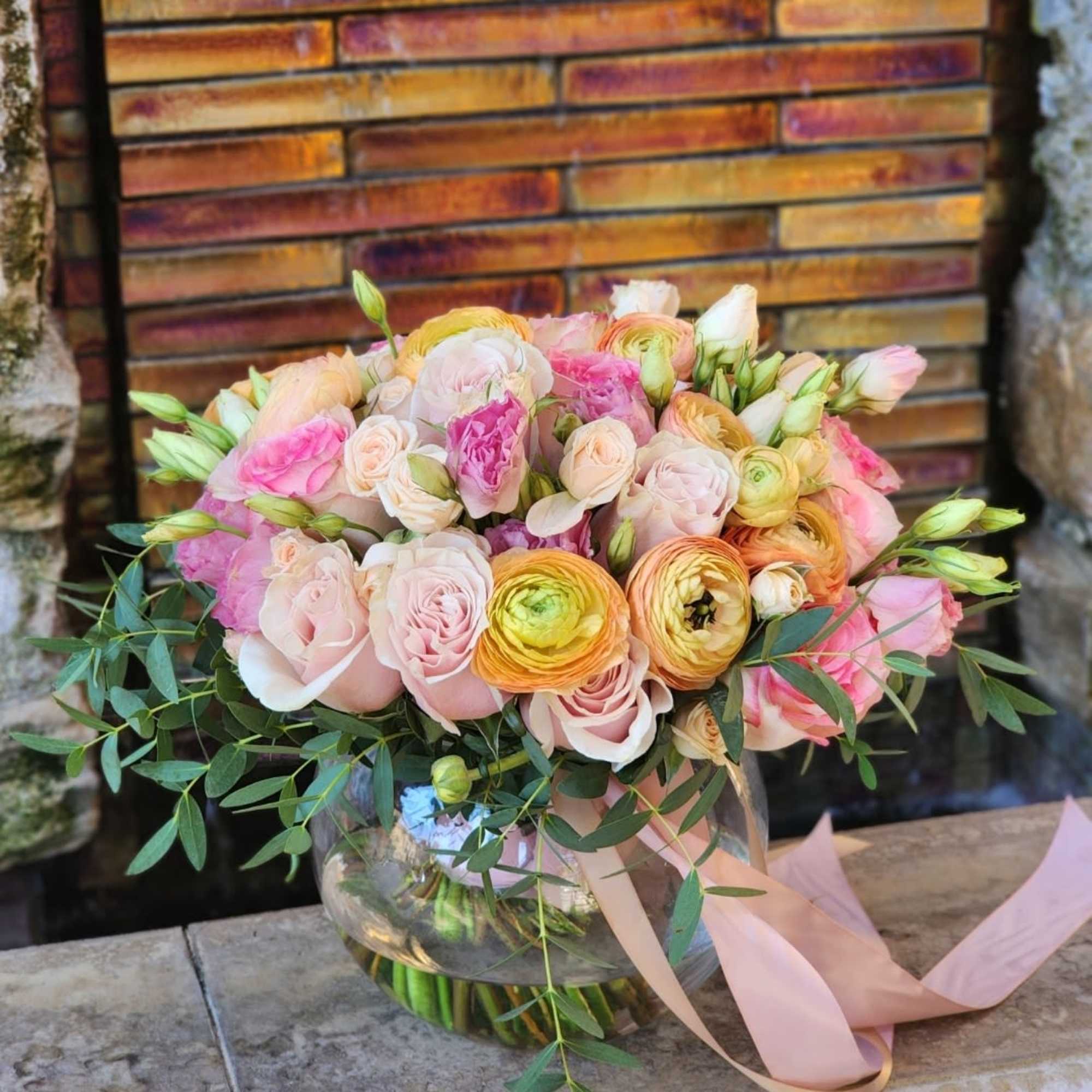  A clear vase arrangement featuring peach Ranunculus, pink roses , and