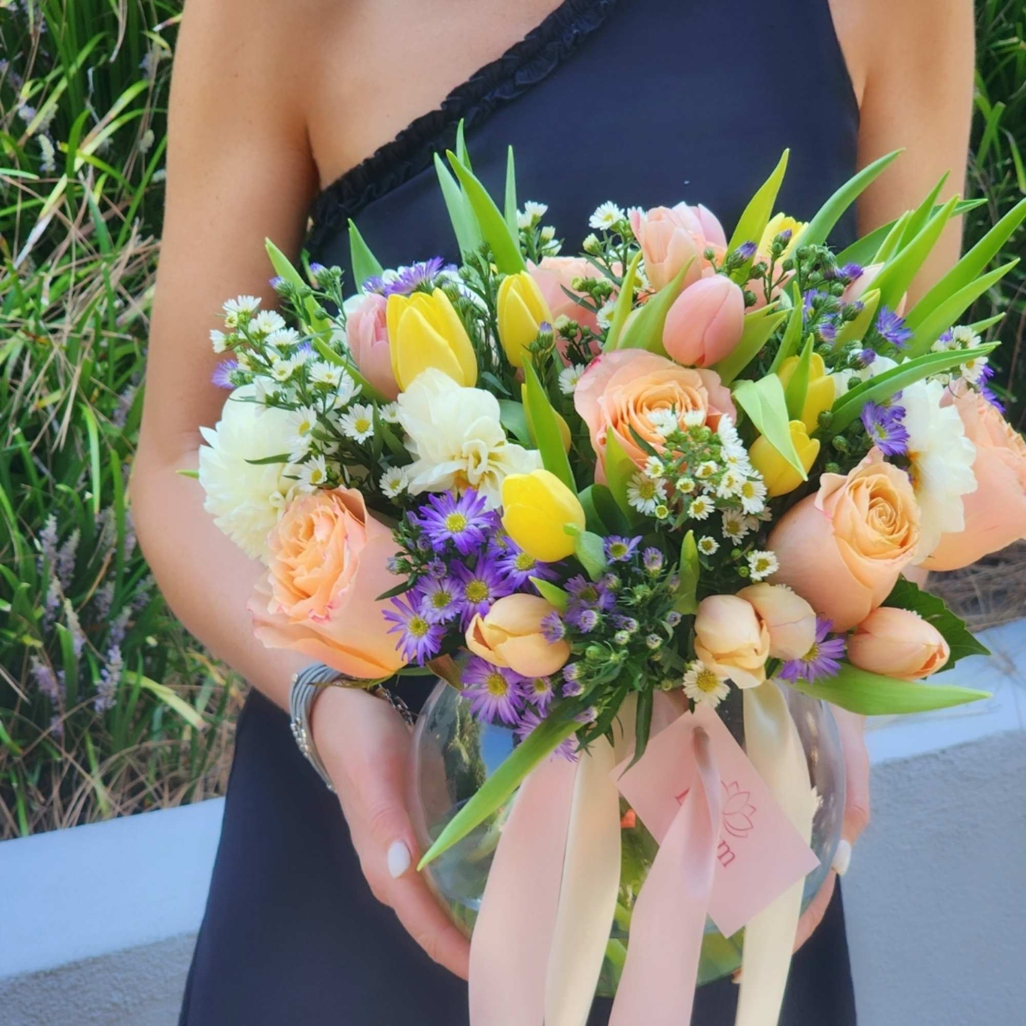  A clear vase arrangement featuring peach roses, yellow tulips, white dahlias