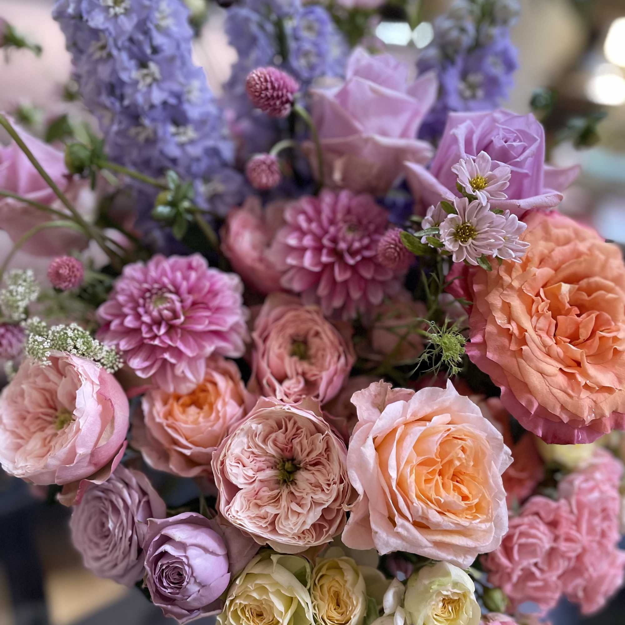 This elegant floral arrangement features delicate roses in soft pastels, vibrant delphiniums