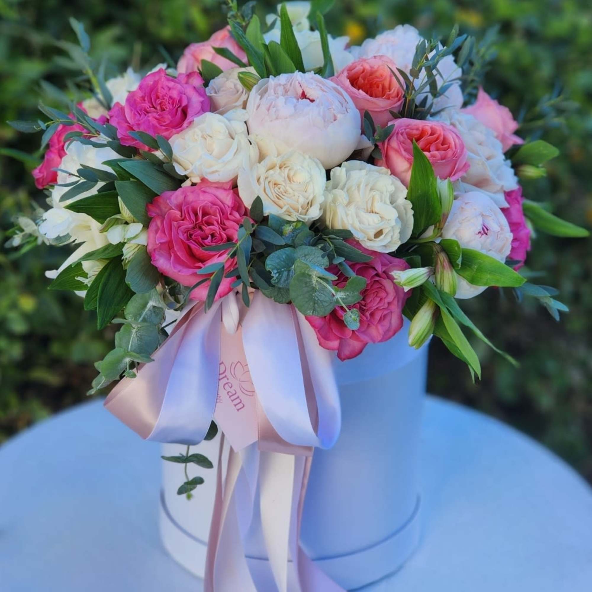 The arrangement in white hatbox features a stunning mix of flowers, including
