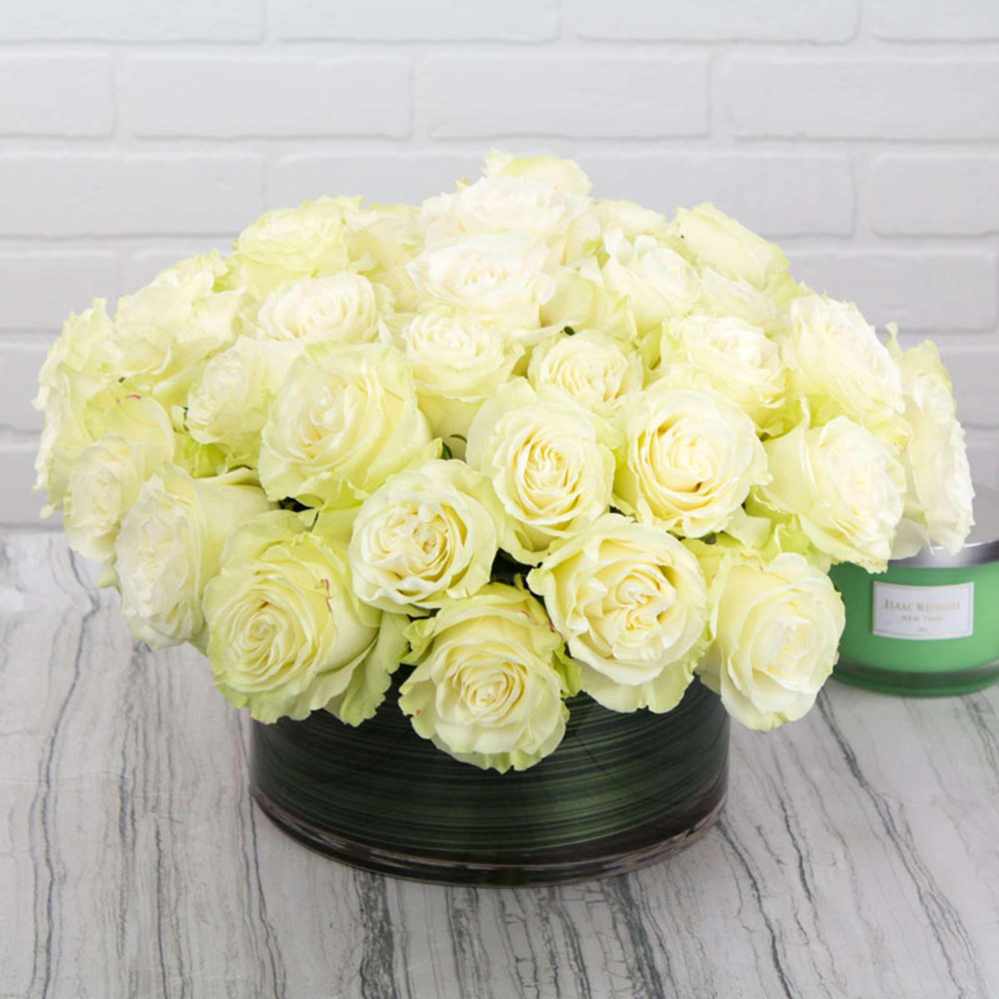 Low round arrangement of pale yellow roses in a glass vase with green lining.
