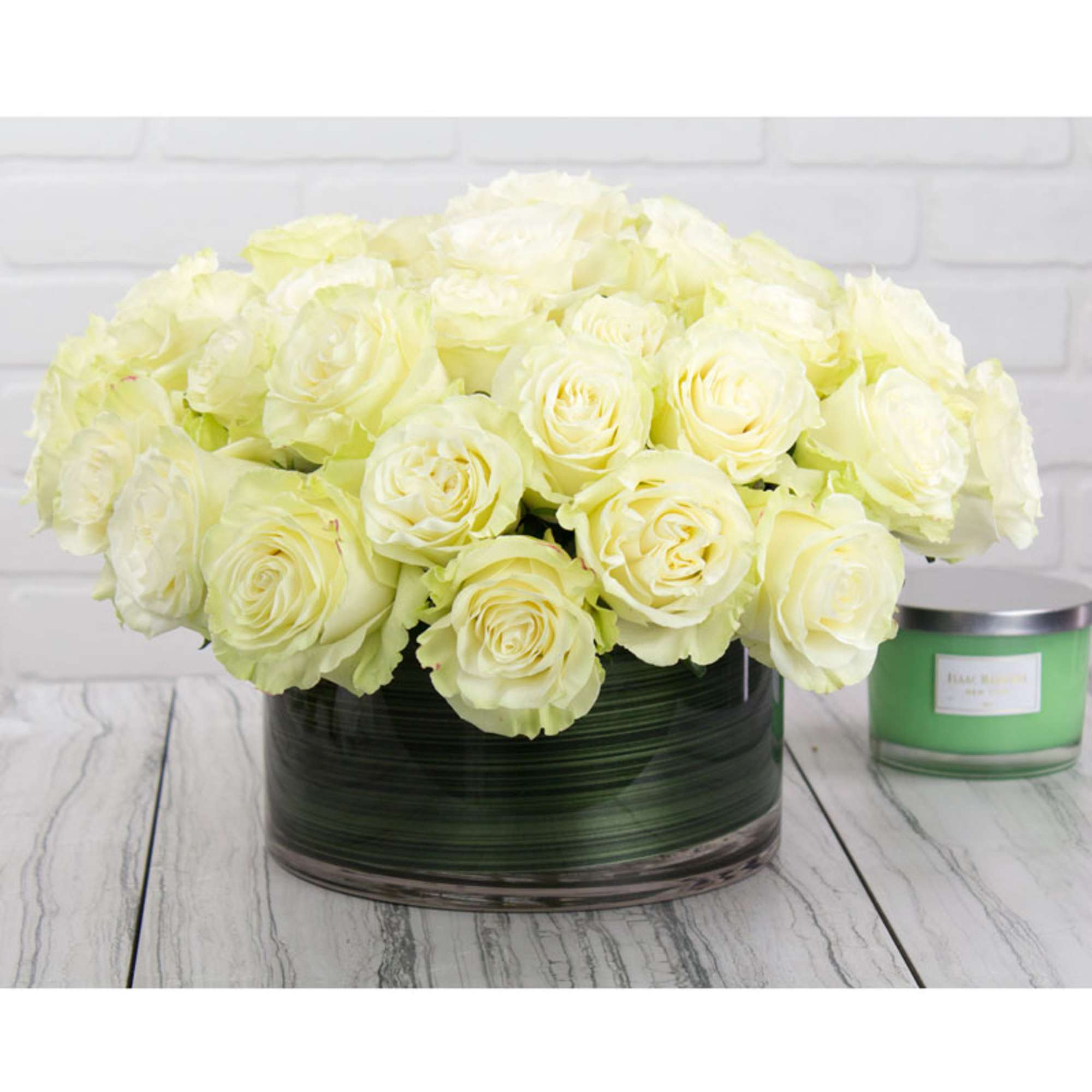 Low round arrangement of pale cream roses in a glass vase on a wood surface