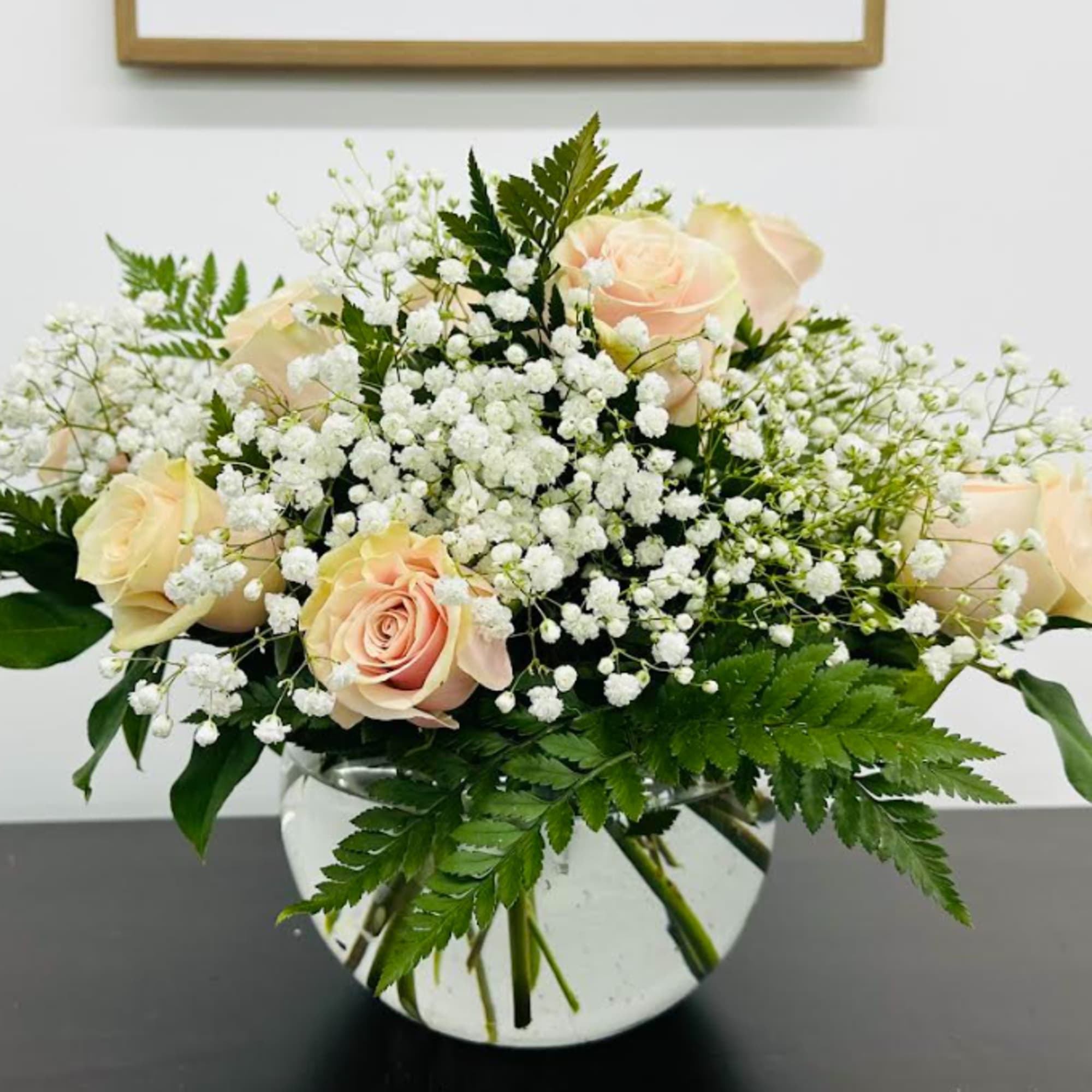 A delicate bowl arrangement of light pink roses with babies breath for