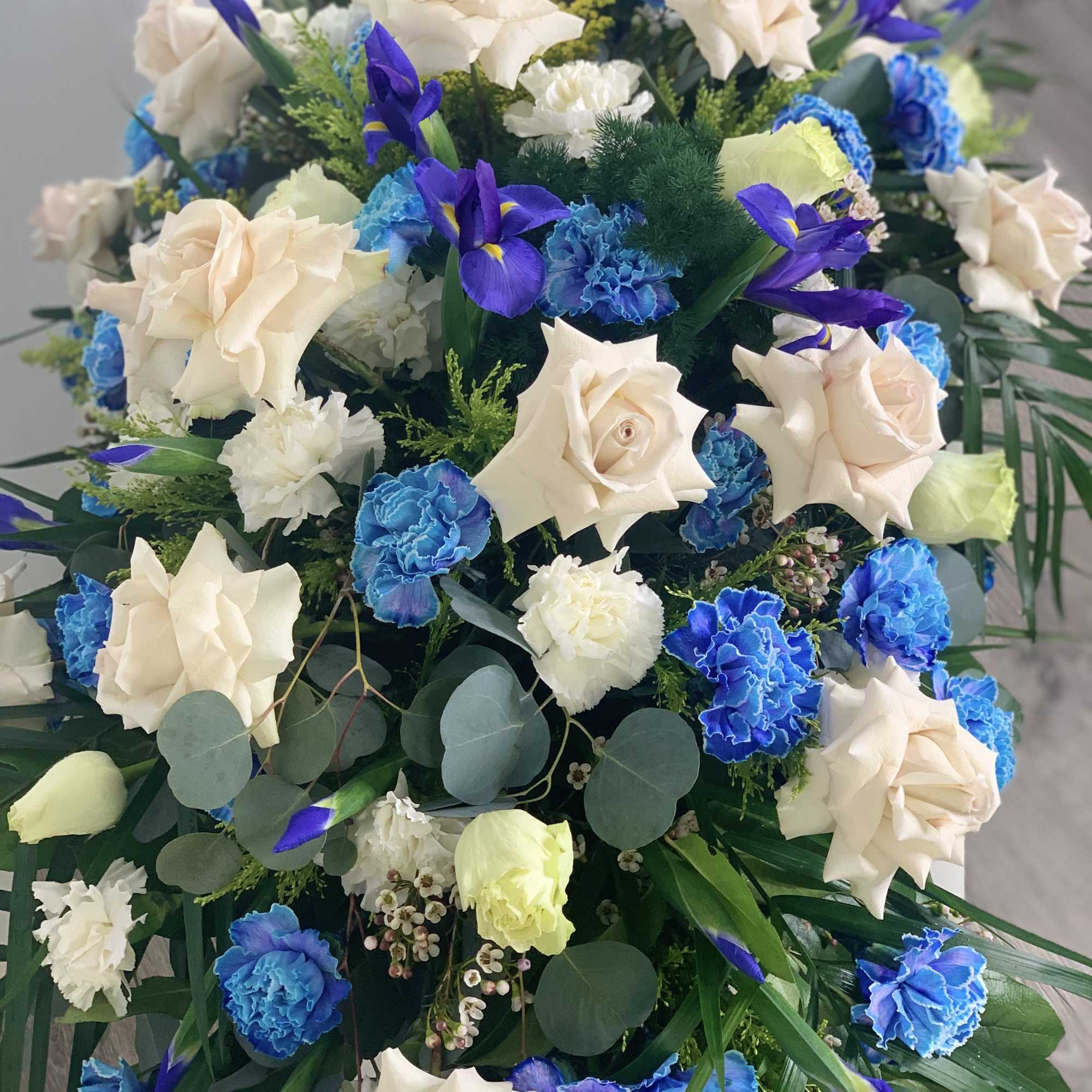 A beautiful casket spray with significant blue flowers that are unique and