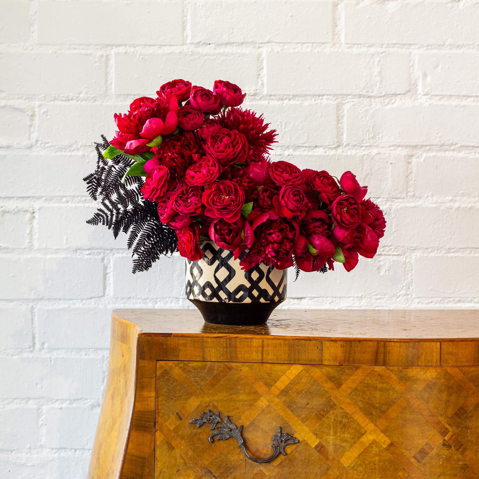 Imagine a striking floral arrangement featuring deep dark burgundy peonies and red