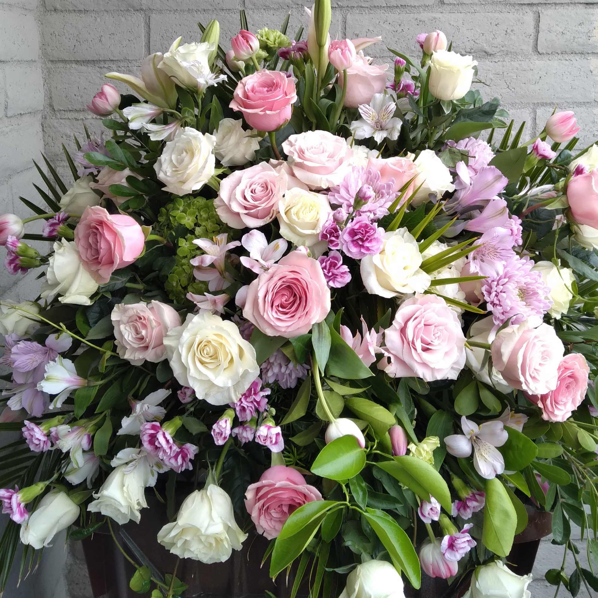 This casket spray is filled with assorted pink seasonal blooms.